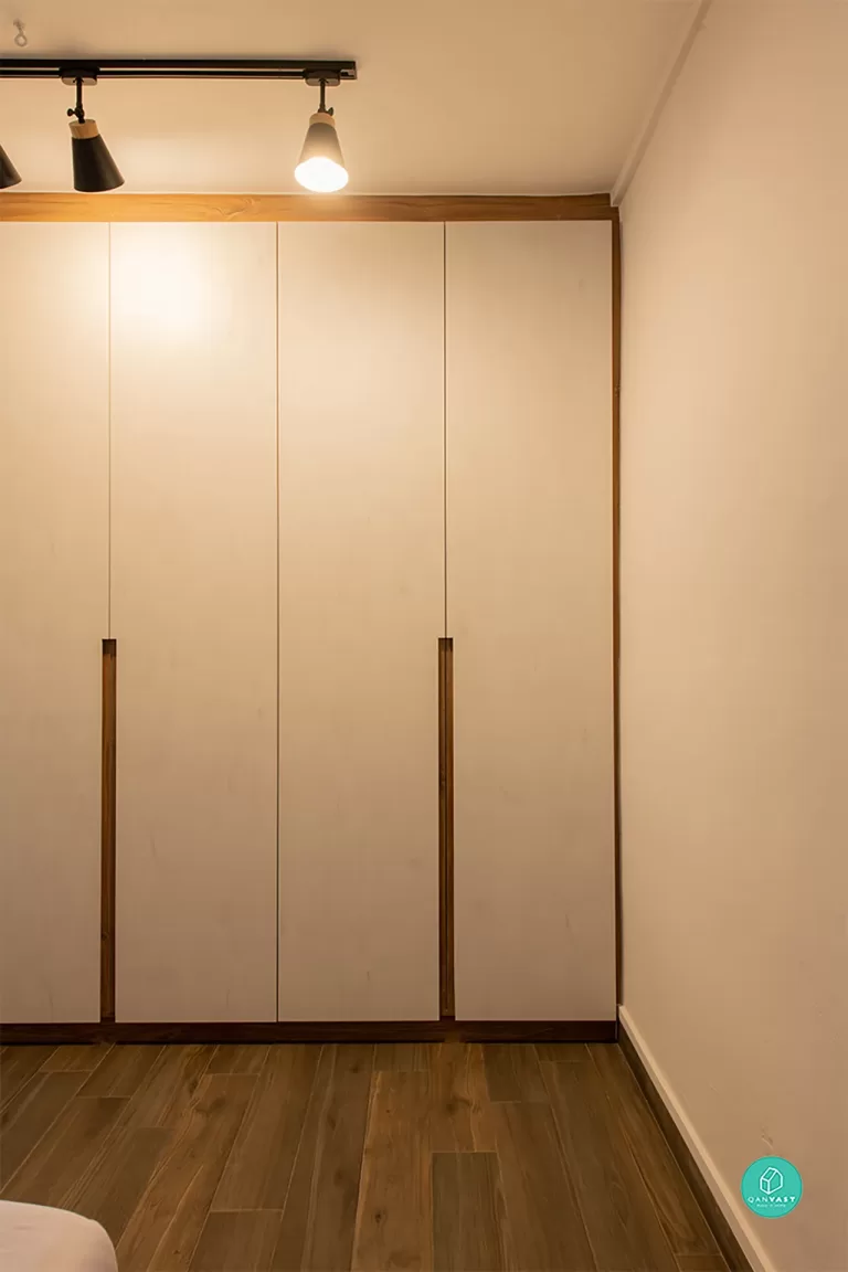 Minimalist HDB bedroom built-in wardrobe in light wood veneer (likely Birch or Ash). Features full-height, handle-less doors with vertical inset handles, providing maximum storage and a clean, serene aesthetic.