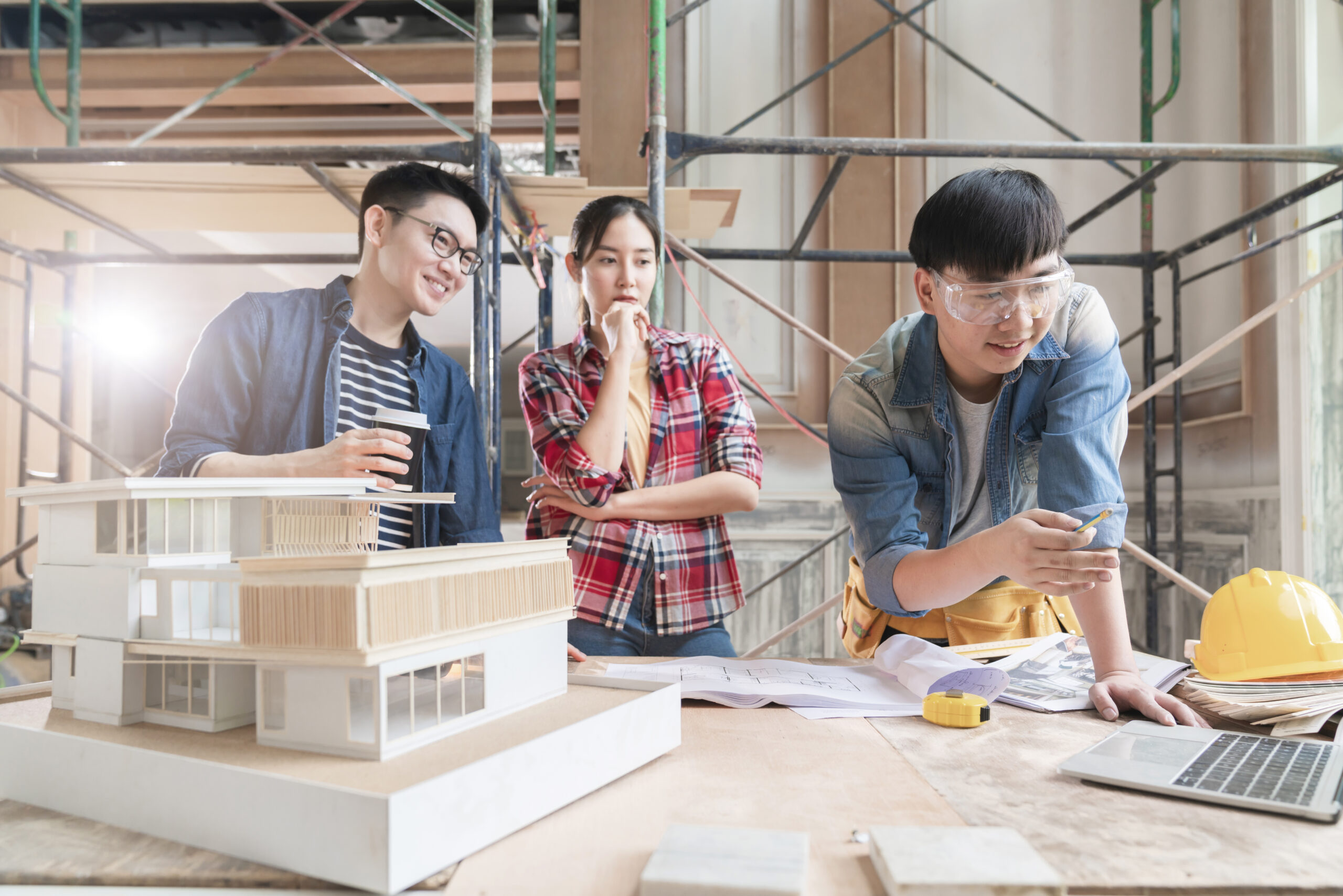 group of smart asian architect interior design team consulting with construction engineer work brainstorm meeting with house project blueprint and home mockup in house renovation structure background.