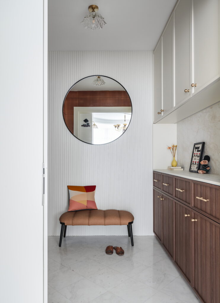 An entrance with a wooden shoe rack, plush seating for changing shoes, and a wall-mounted mirror for quick outfit checks before going out.