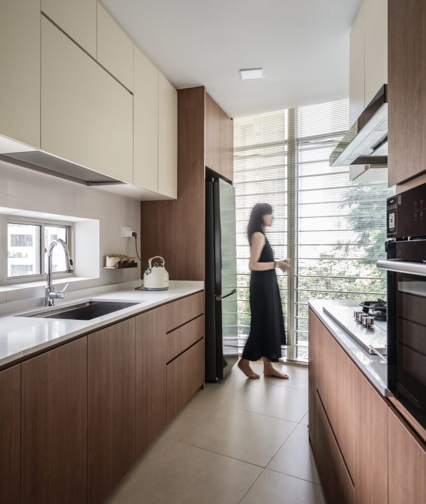 A lady relaxing in a kitchen next to a sleek, large black fridge. The kitchen features wooden and beige cabinets and offers a breathtaking view.