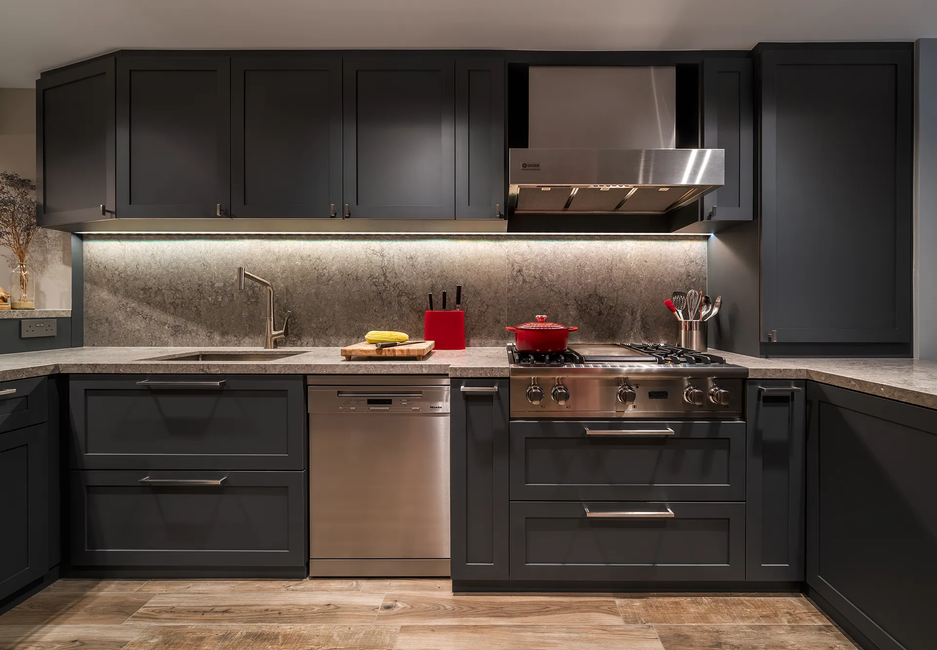 A compact HDB kitchen with dark gray cabinets, a textured stone backsplash, and a red pot on a gas stove at 110 Bukit Purmei.