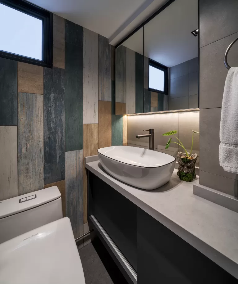 A modern HDB bathroom at 110 Bukit Purmei with a white vessel sink on a gray counter and a unique wooden-paneled accent wall.