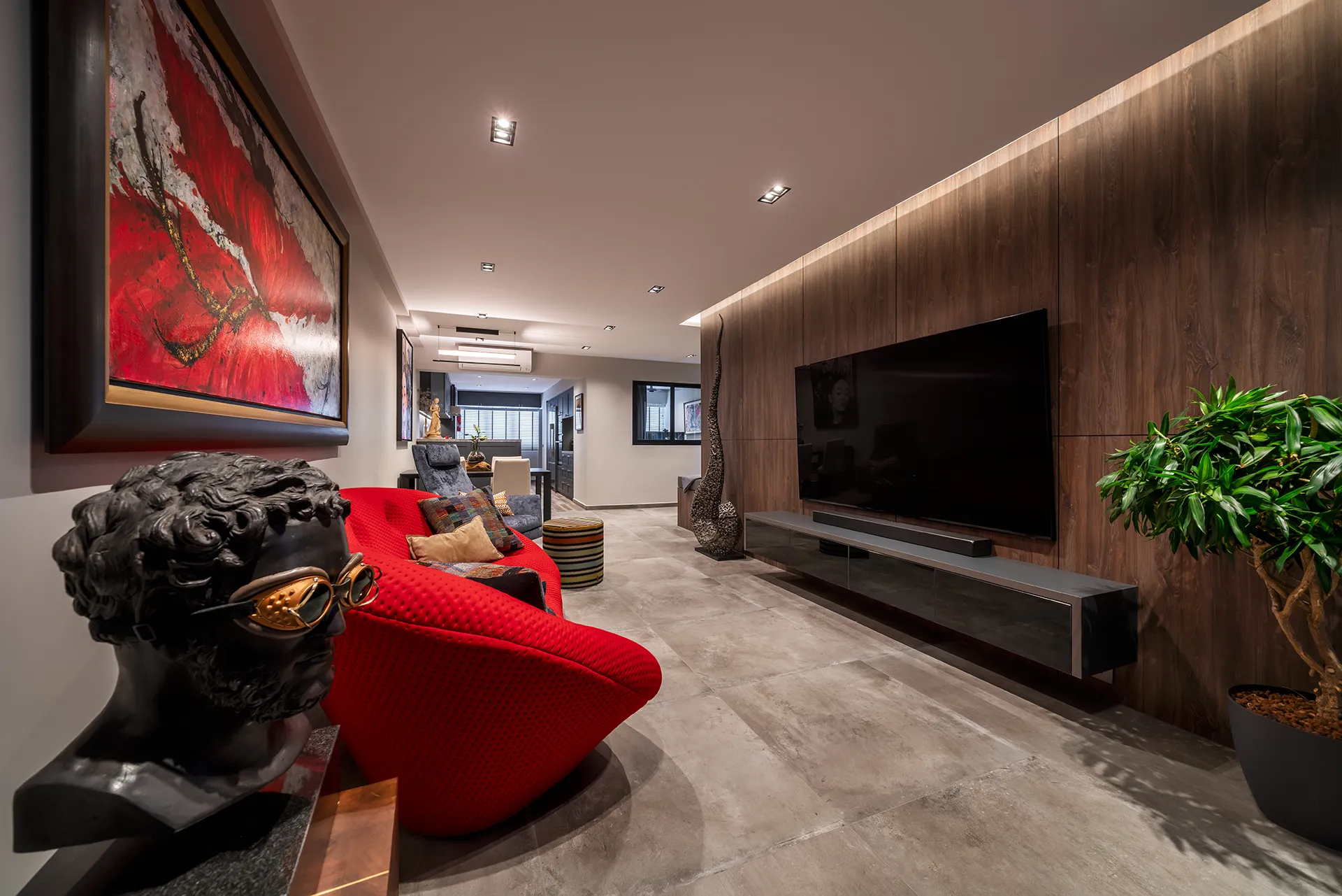 A modern HDB living room at 110 Bukit Purmei featuring a red armchair, a TV on a wooden accent wall, and a black floating console.