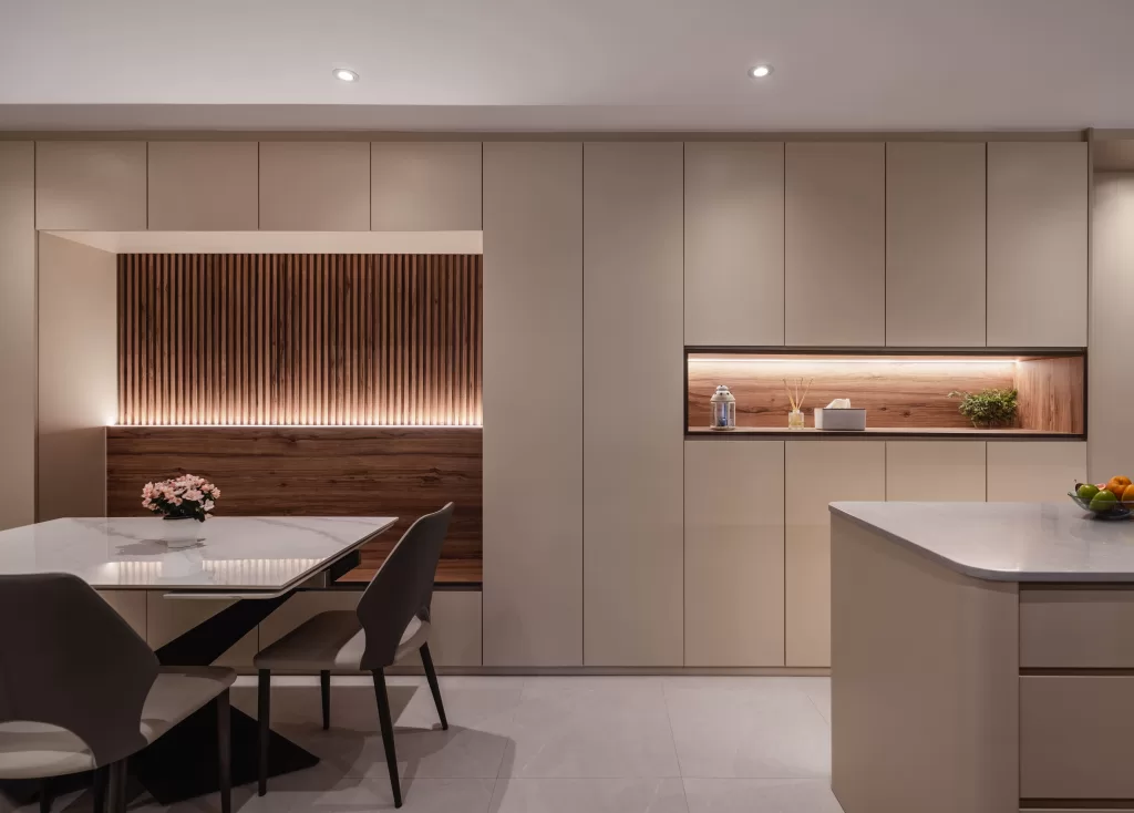 An open-concept dining area with seamless beige cabinets, a recessed wood-lined seating nook, and a white dining table.