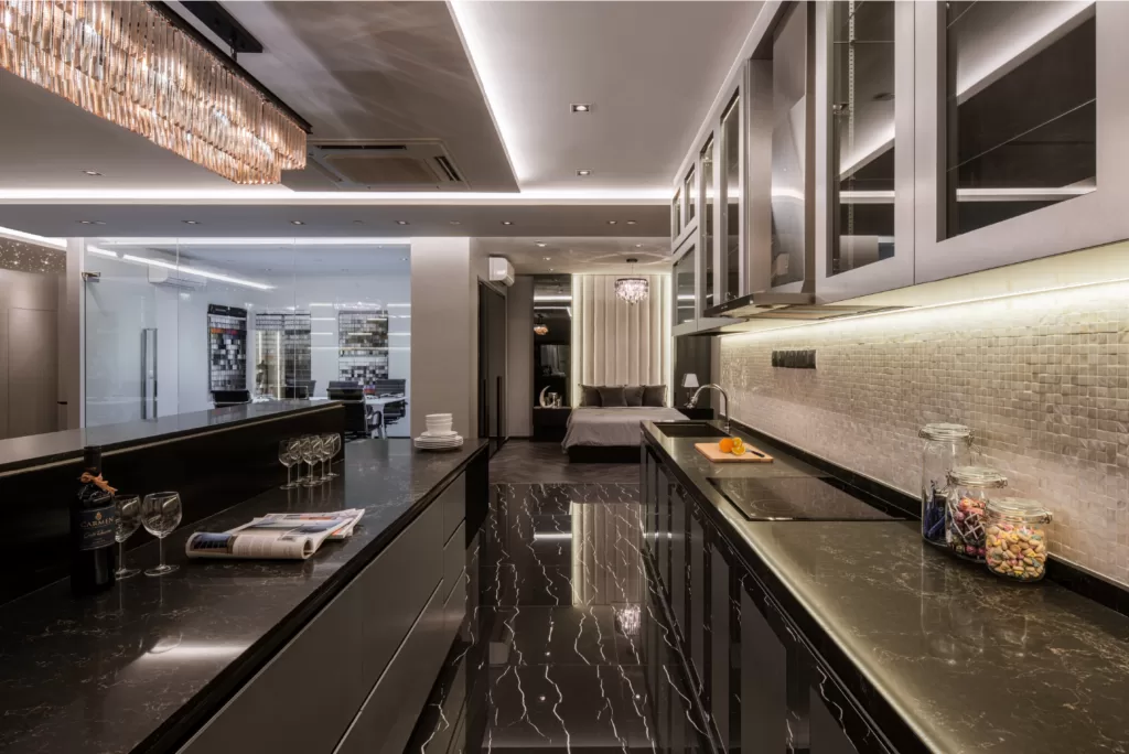 Open-plan modern kitchen with sleek black countertops, glossy cabinetry, and kitchen island featuring white plates and wine glasses, adjacent to a stylish living area at 37 Jalan Pemimpin.