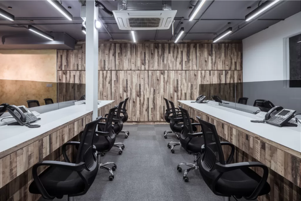 Professional office workspace with white desks, black ergonomic chairs, telephones, and wood-paneled walls under bright overhead lighting at 37 Jalan Pemimpin.