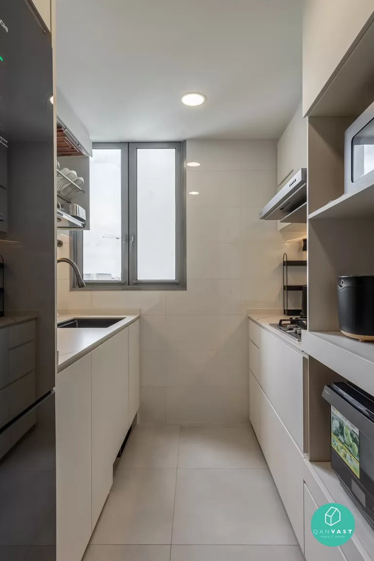 A minimalist and streamlined kitchen at Bartley Ridge with white, handle-free cabinetry and glossy white wall tiles. The image shows a black refrigerator, a stainless steel sink under a window, and a built-in stovetop, emphasizing modern urban efficiency.
