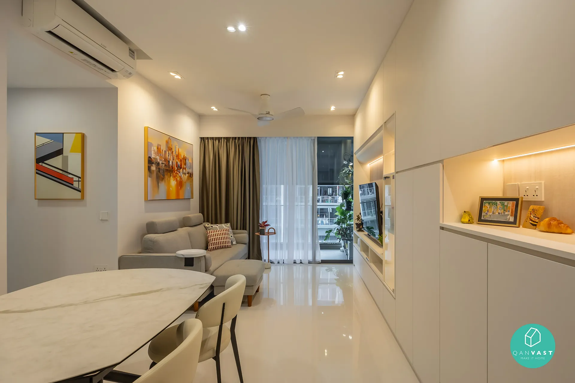 A modern open-concept living and dining area at Bartley Ridge featuring a grey sectional sofa and a wall-mounted TV in a recessed unit with accent lighting. The image includes a round dining table and a ceiling fan, highlighting a cohesive and airy space.