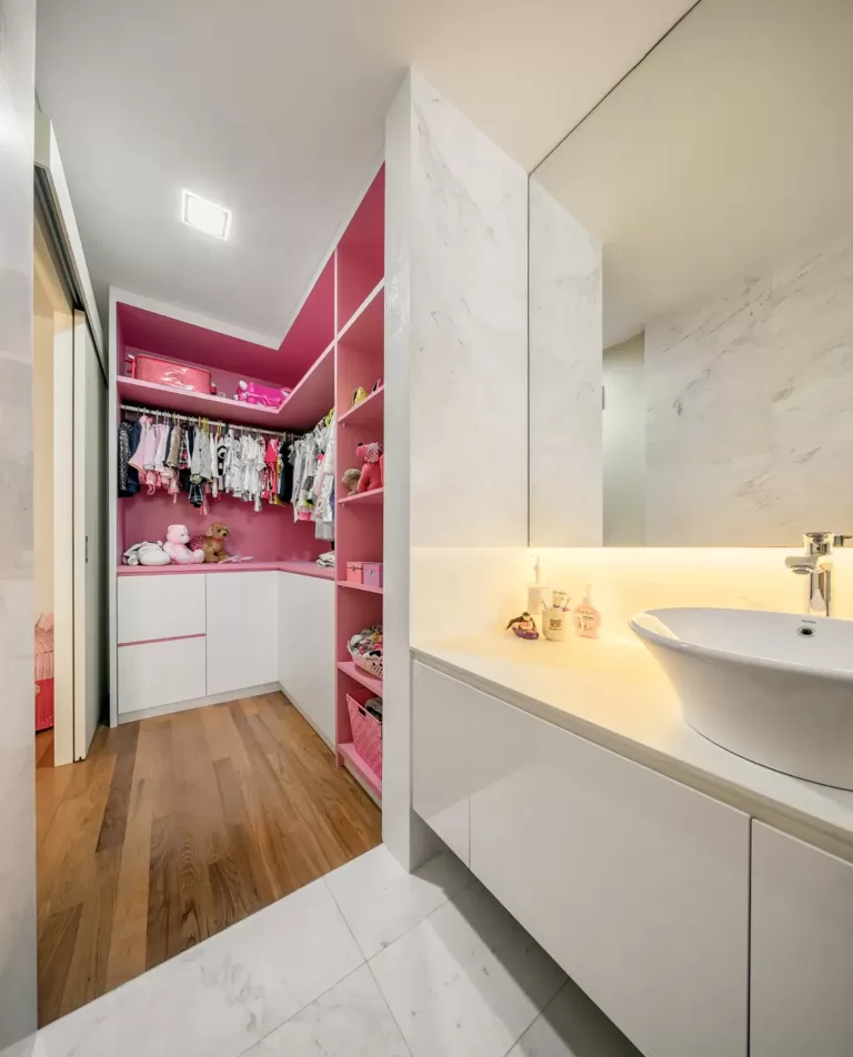 A child’s walk-in closet and vanity area in a Greenbank Park residence, showcasing a clean white and soft pink closet interior with organized clothes and toys, and a marble-tiled vanity with a vessel sink.