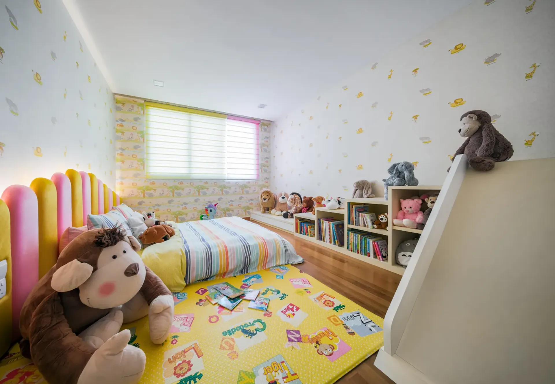 A whimsical kids' bedroom in a Greenbank Park, Singapore home, featuring an indoor slide attached to a white bookshelf filled with toys, a striped bedspread, and a colorful play mat.