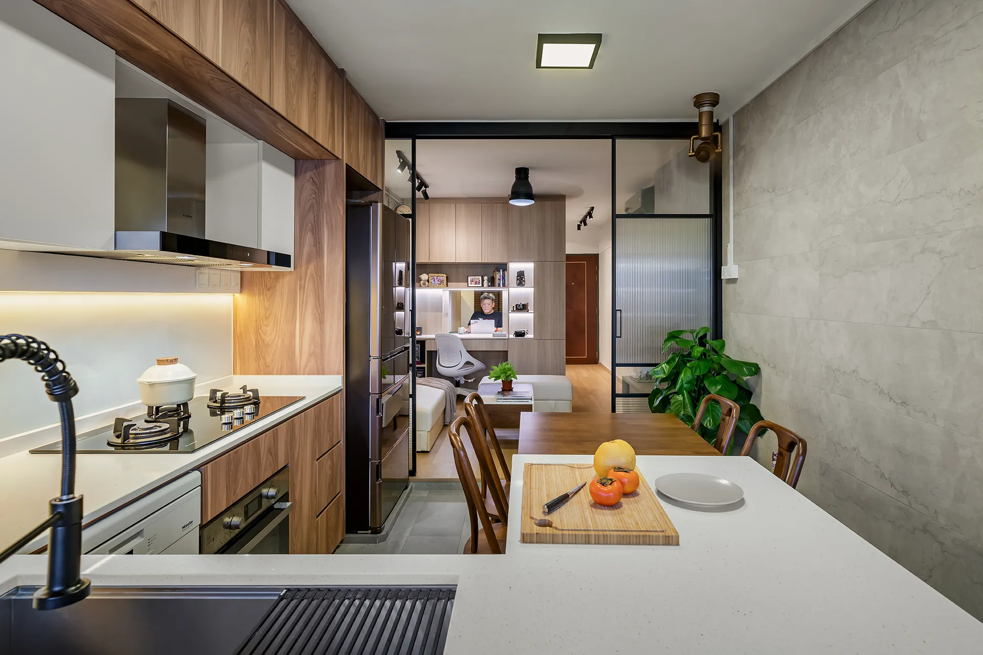 Minimalist kitchen and dining with warm wood cabinetry, matte black refrigerator, white countertop, wood dining table, and black glass partition in Clementi HDB.