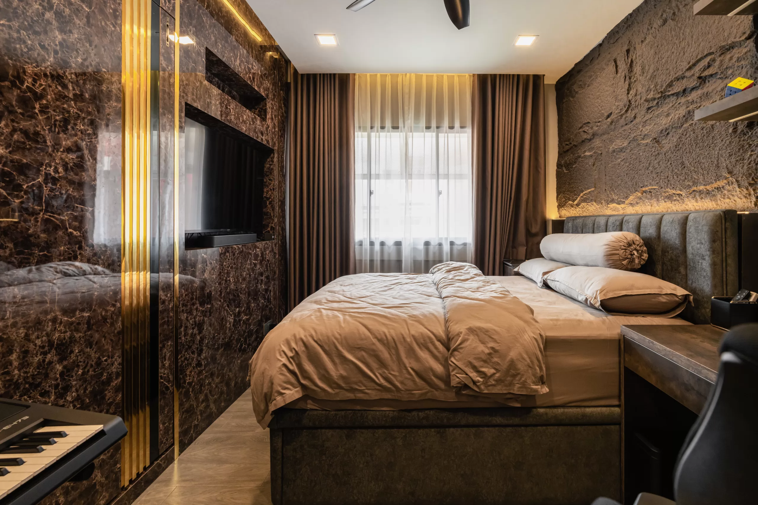 609 Elias Road, 5-room HDB, Modern Luxury bedroom. Contrast between a textured stone headboard wall and a glossy dark marble TV wall, with an integrated workspace.