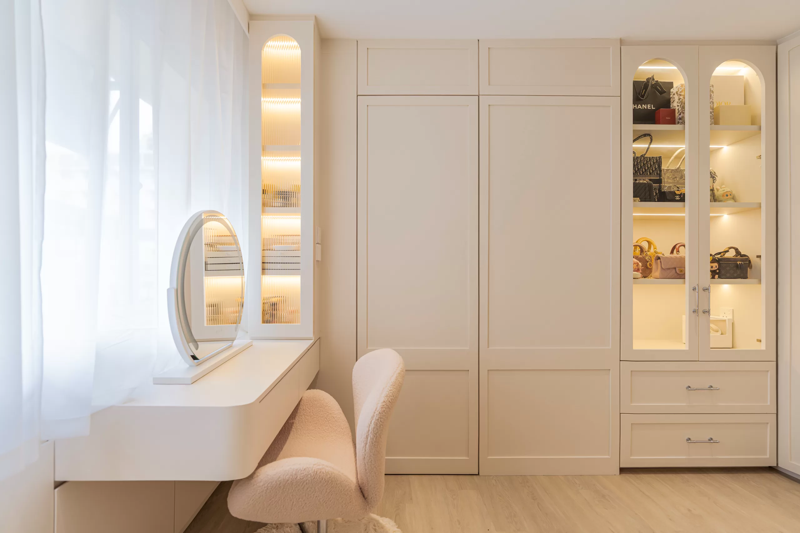 Elegant minimalist dressing room in the 4-room HDB featuring a round illuminated vanity mirror and glass-fronted cabinets for displaying designer accessories.