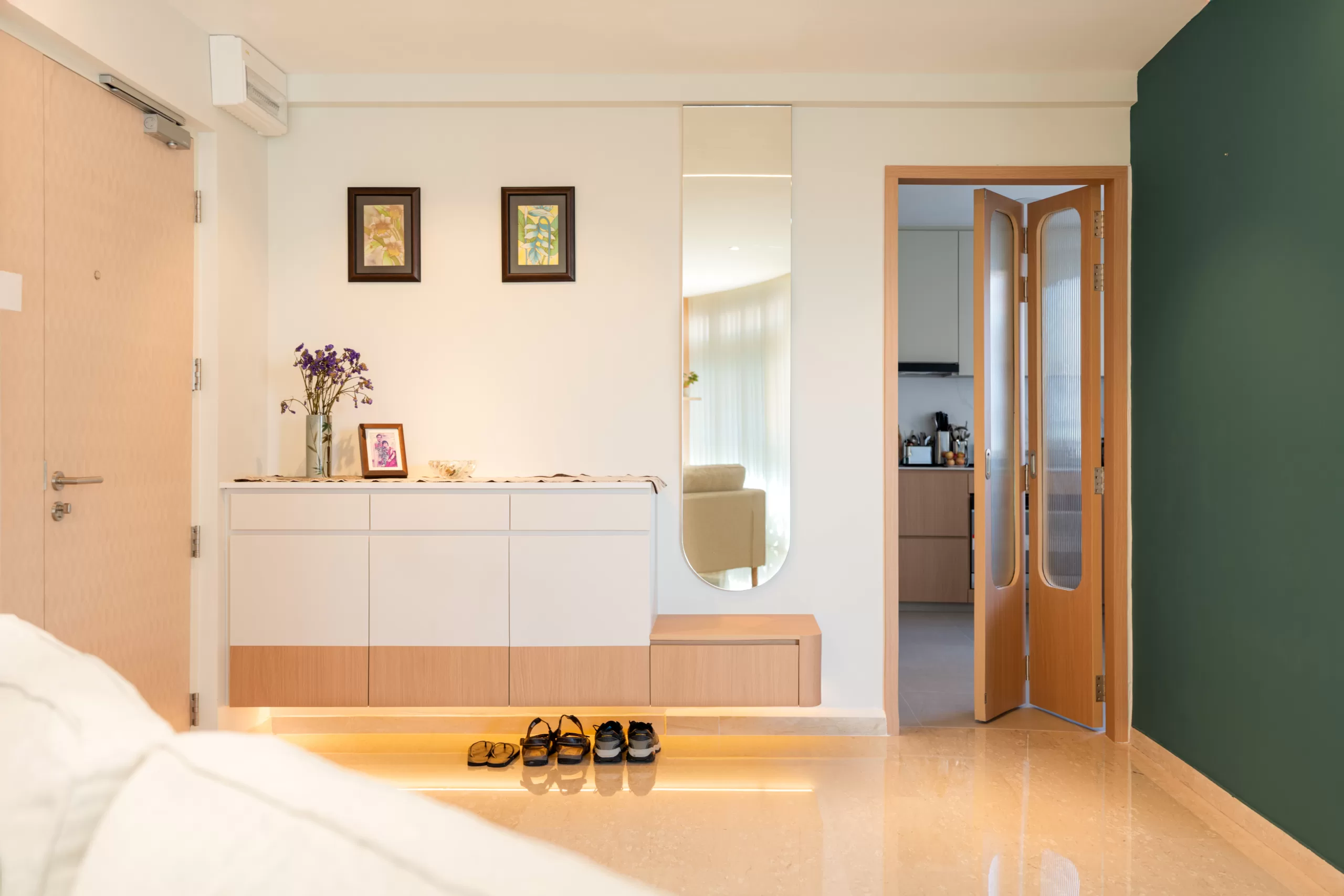 Japandi HDB entryway featuring a low white and light wood floating cabinet, vertical mirror, and a deep green accent wall for material contrast.