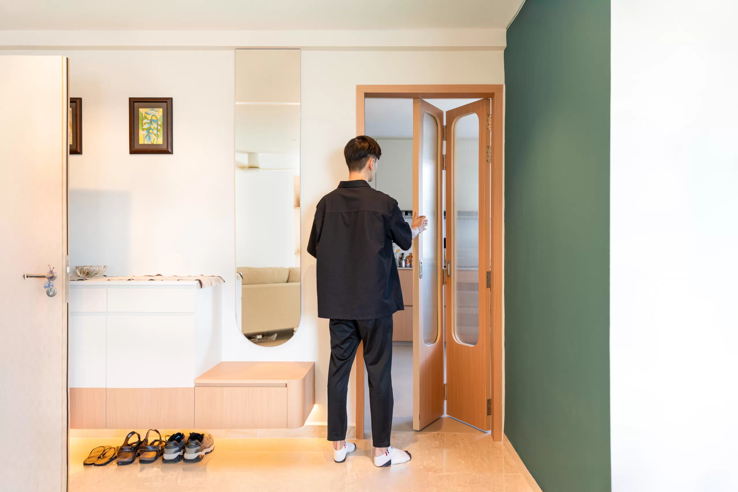 Minimalist HDB entryway with a wooden folding door, vertical mirror, and green accent wall, emphasizing clean design and functional space-saving.