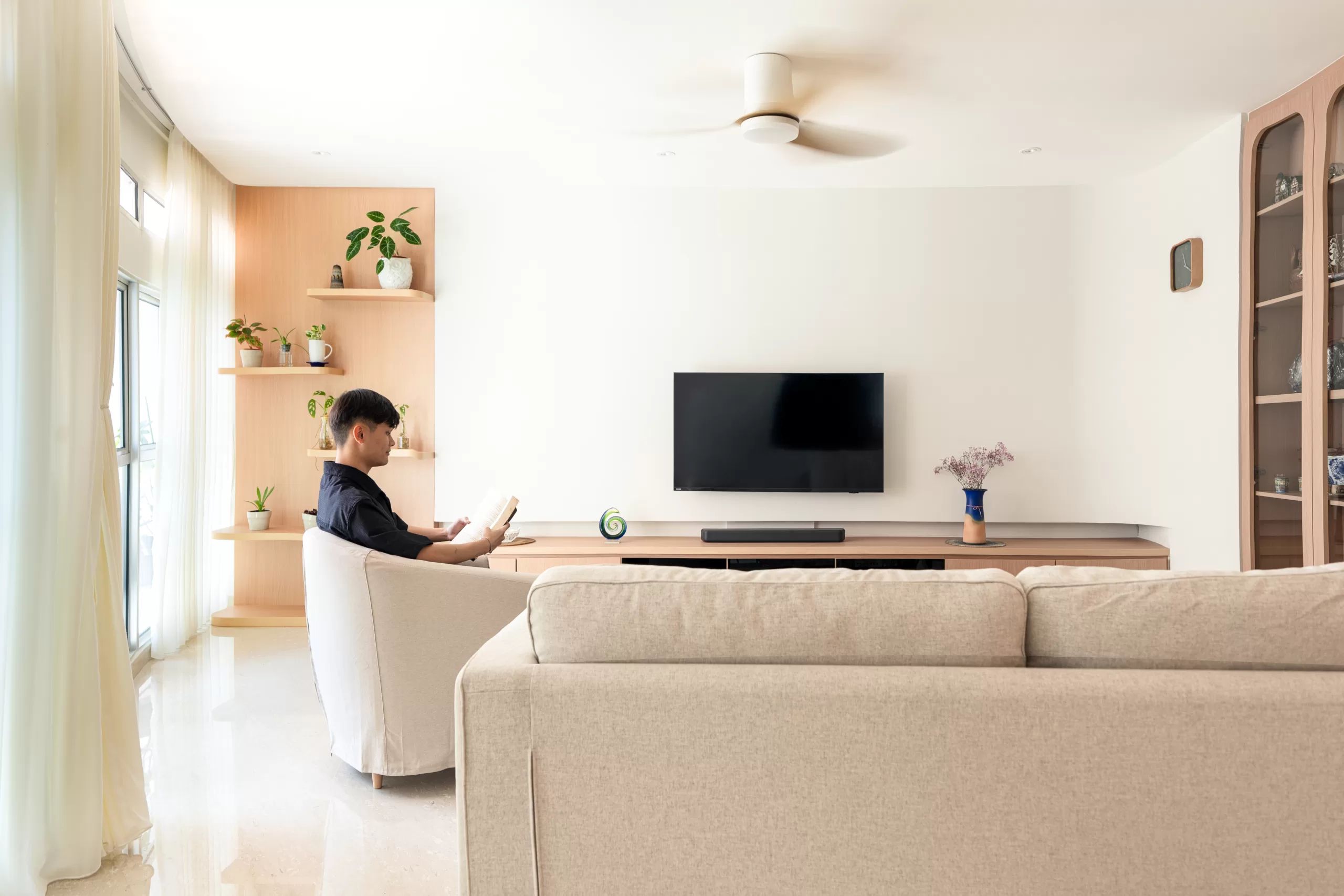 Symmetrical Japandi living room layout with two grey sofas, media console, wooden ceiling fan, and extensive vertical shelving with indoor plants.