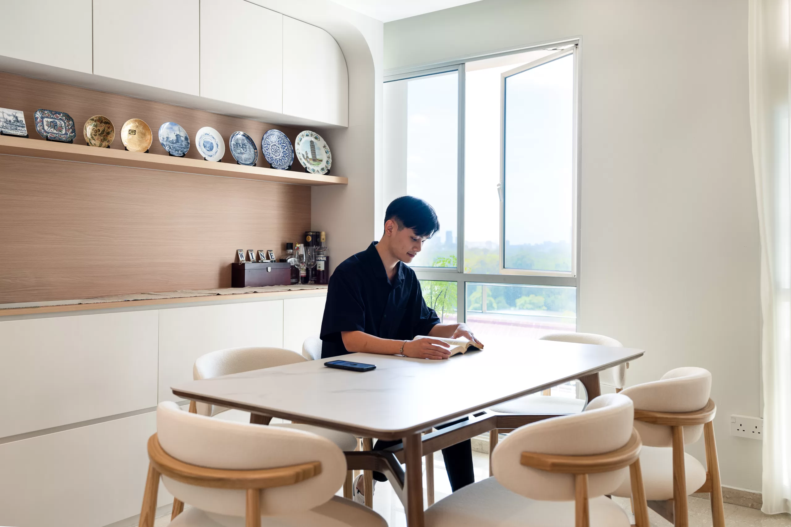 Japandi dining space with a light wooden table and cushioned chairs, featuring a white cabinet with a wood countertop and curated bar/plate display setup.
