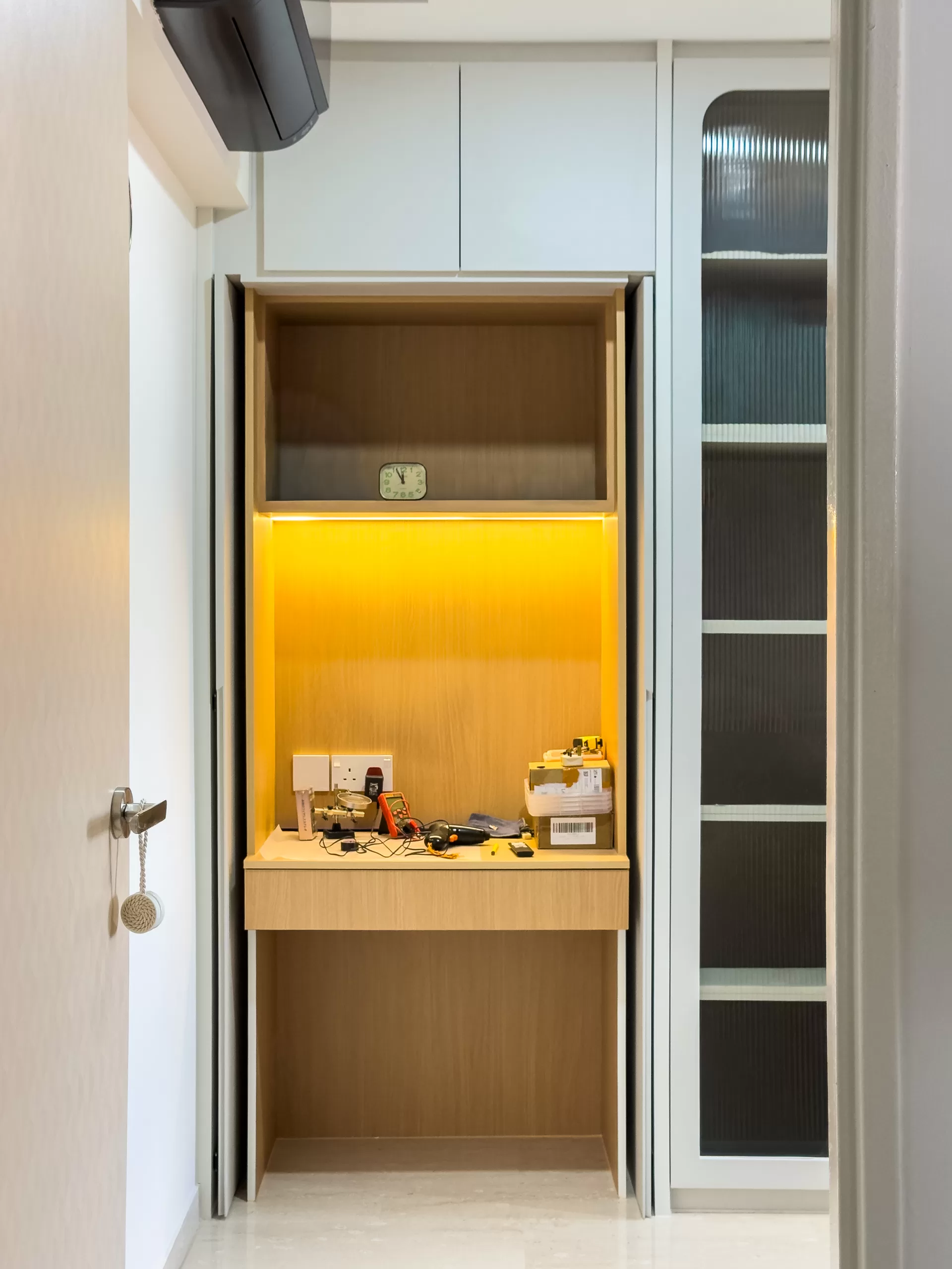 Compact Japandi built-in wooden work alcove for technical tasks, illuminated by warm yellow task lighting and framed by white cabinetry.