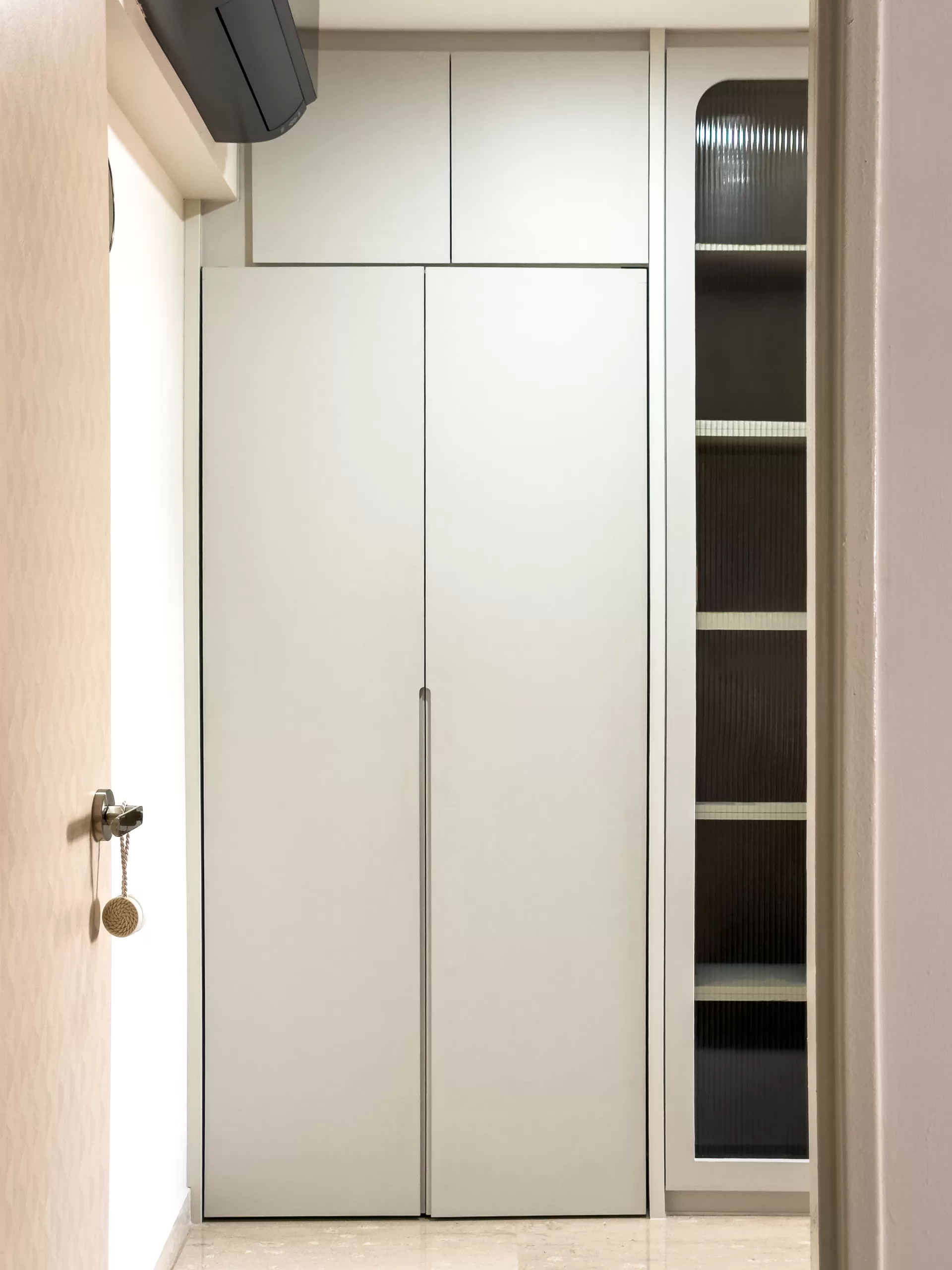 Full-height Japandi wardrobe in light gray matte finish with integrated handles and adjacent display cabinet featuring ribbed/textured glass panels.