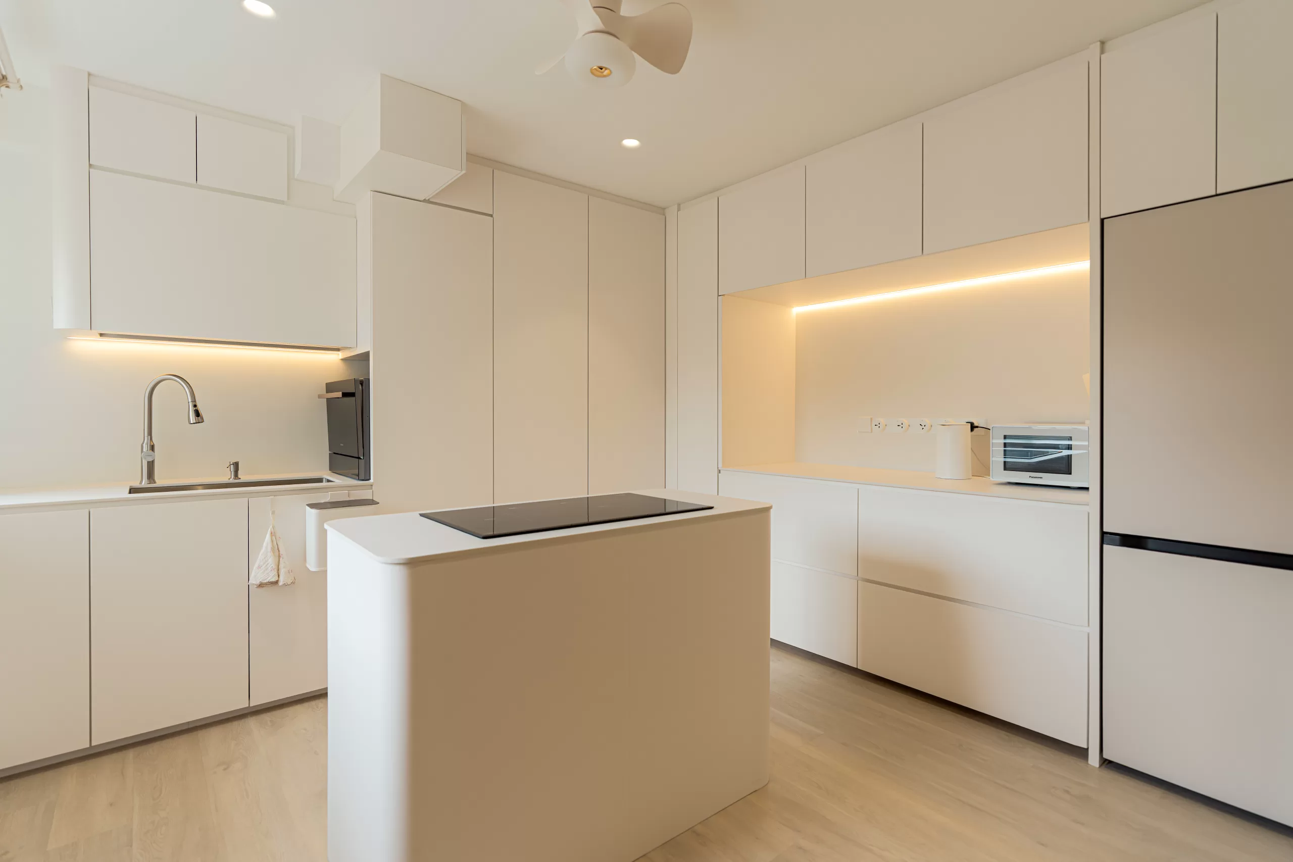 Streamlined minimalist kitchen with white flat-panel cabinetry, light wood flooring, and an integrated cooktop on the island, showcasing clean lines.