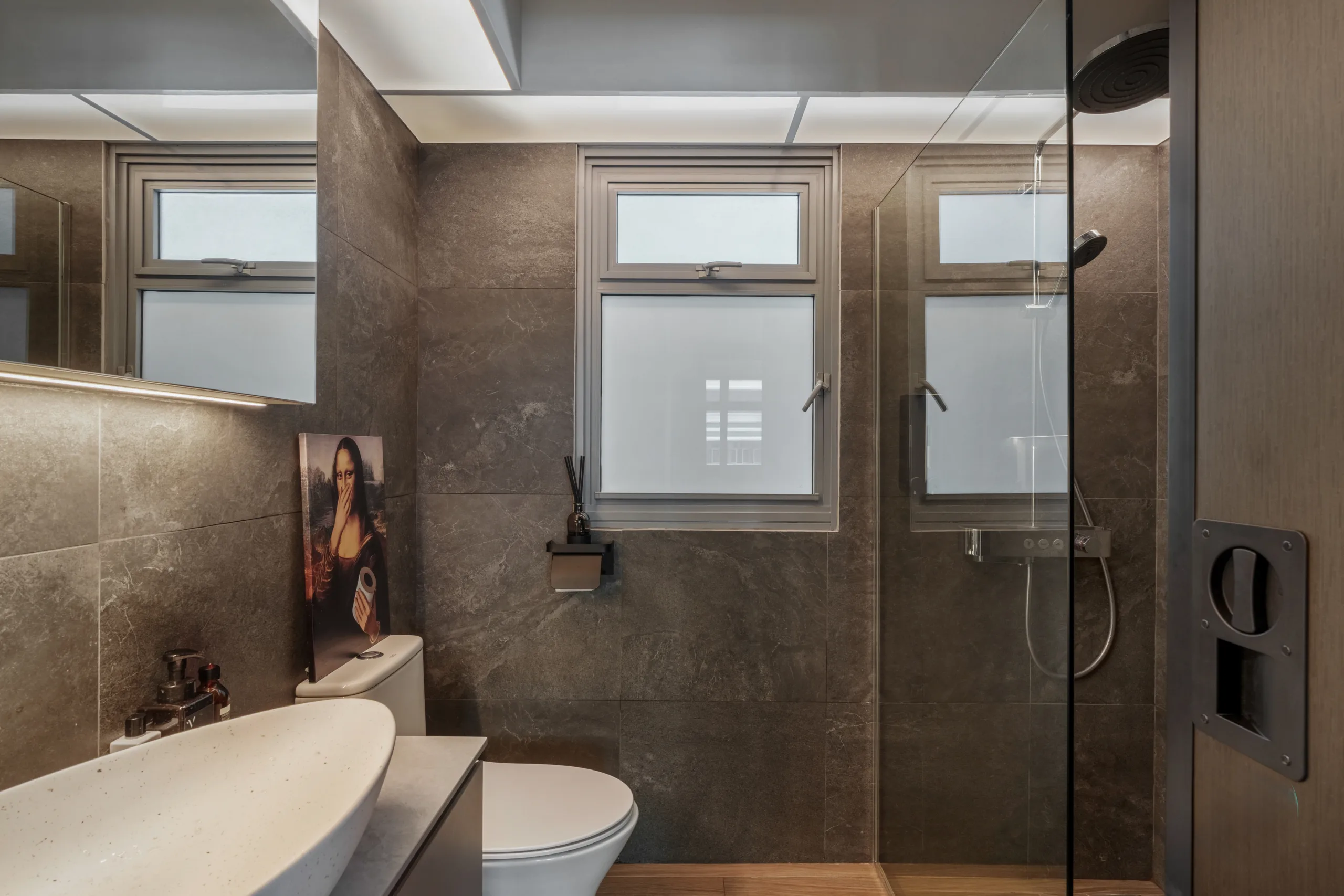 Modern bathroom at Kebun Baru Edge featuring dark stone tiles and humorous Mona Lisa toilet paper artwork.
