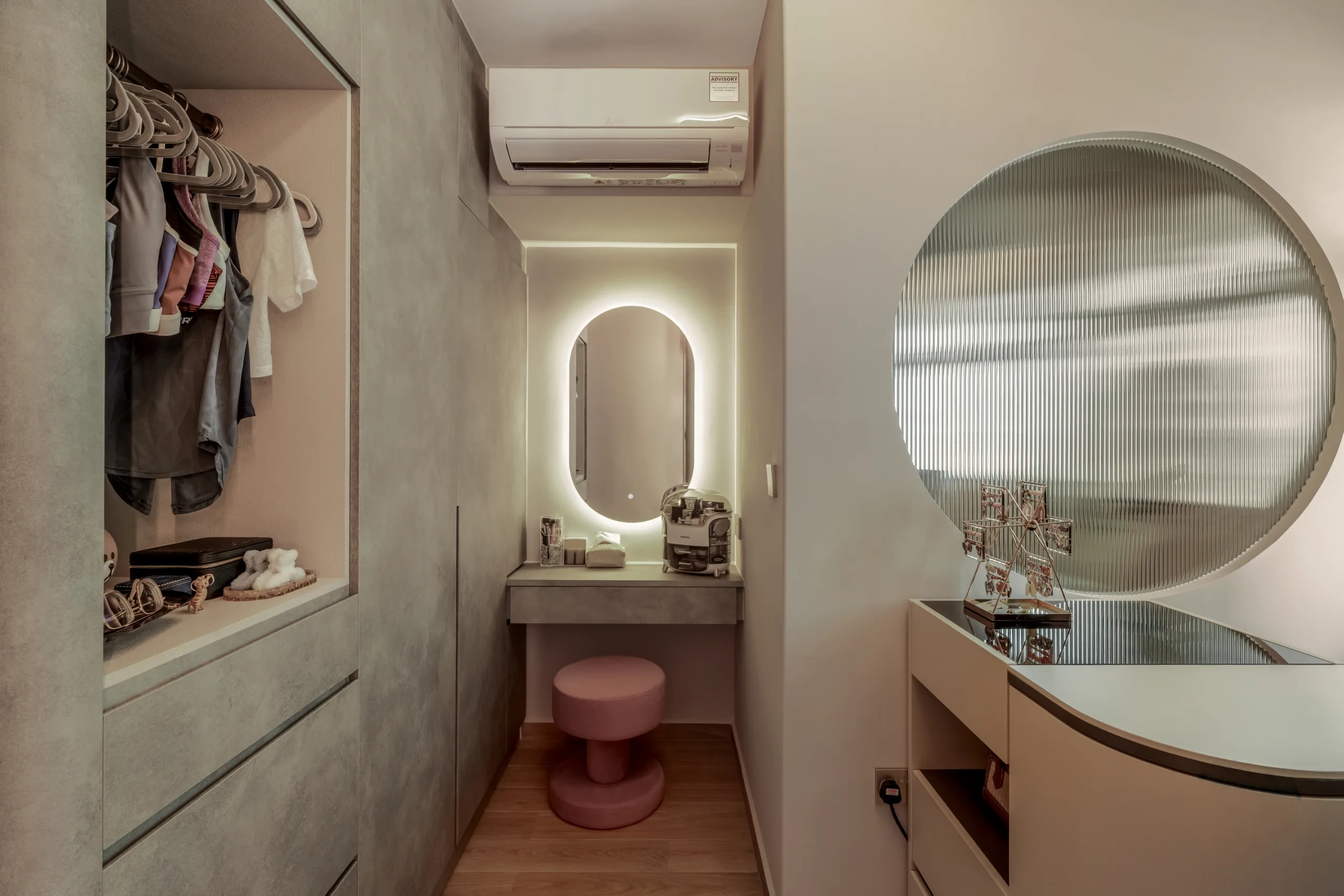 Modern vanity area with a concrete-texture countertop, pink stool, and oval backlit mirror.