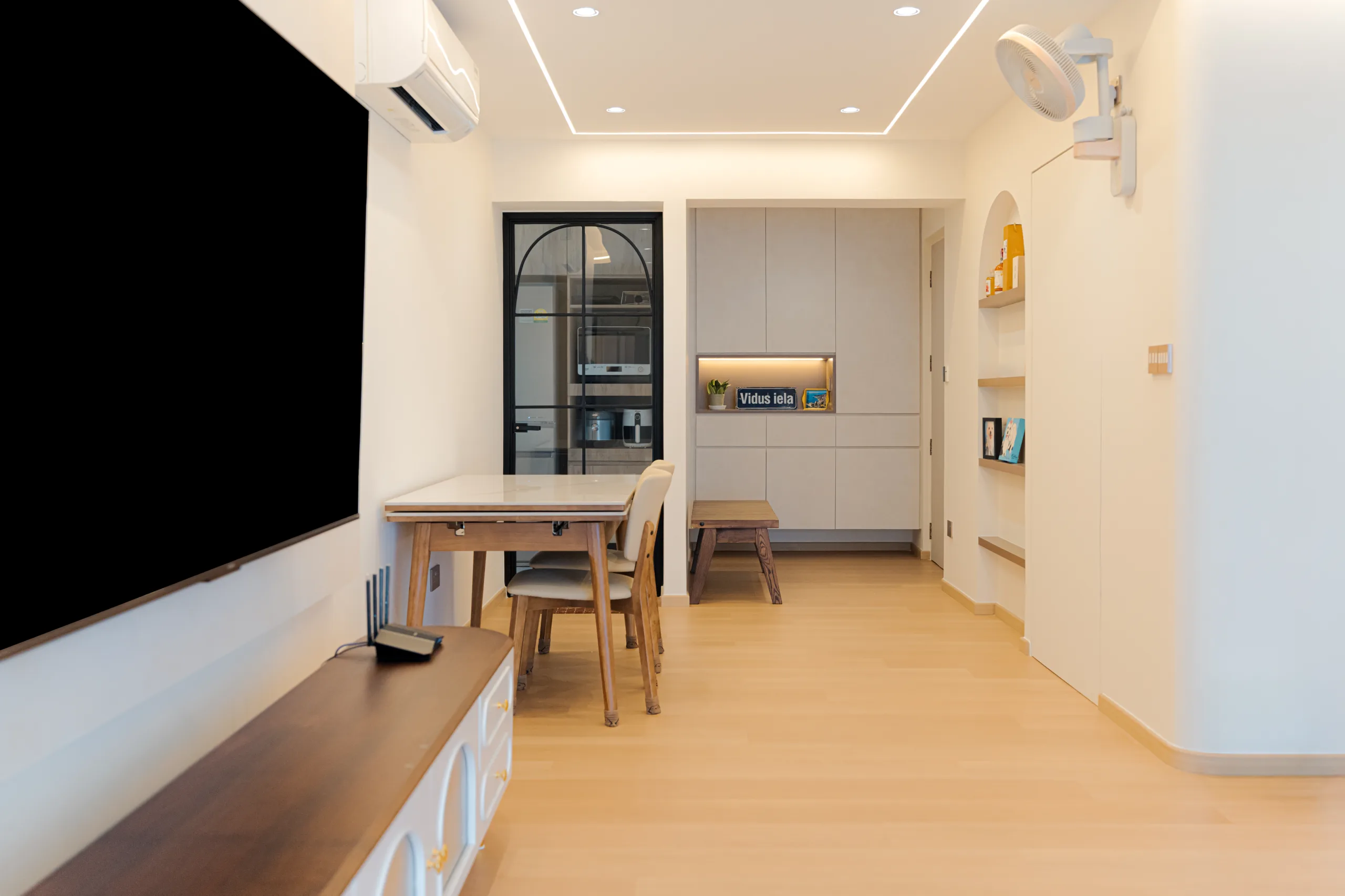Wide-angle view of a 4-room HDB living and dining area with light oak flooring and a glass kitchen door.