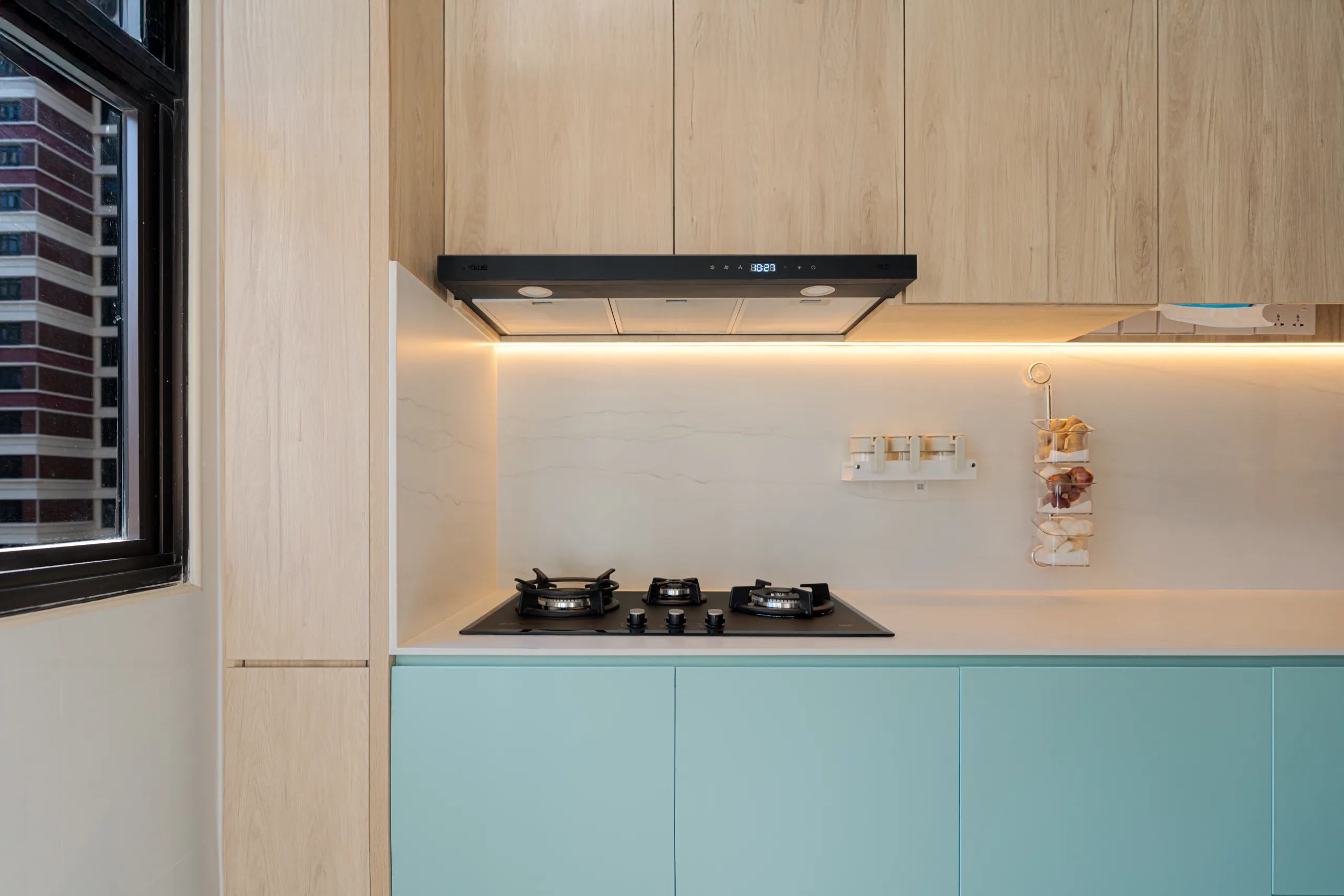 Modern HDB kitchen design with pastel turquoise upper cabinets, light wood lowers, and a built-in gas stove.