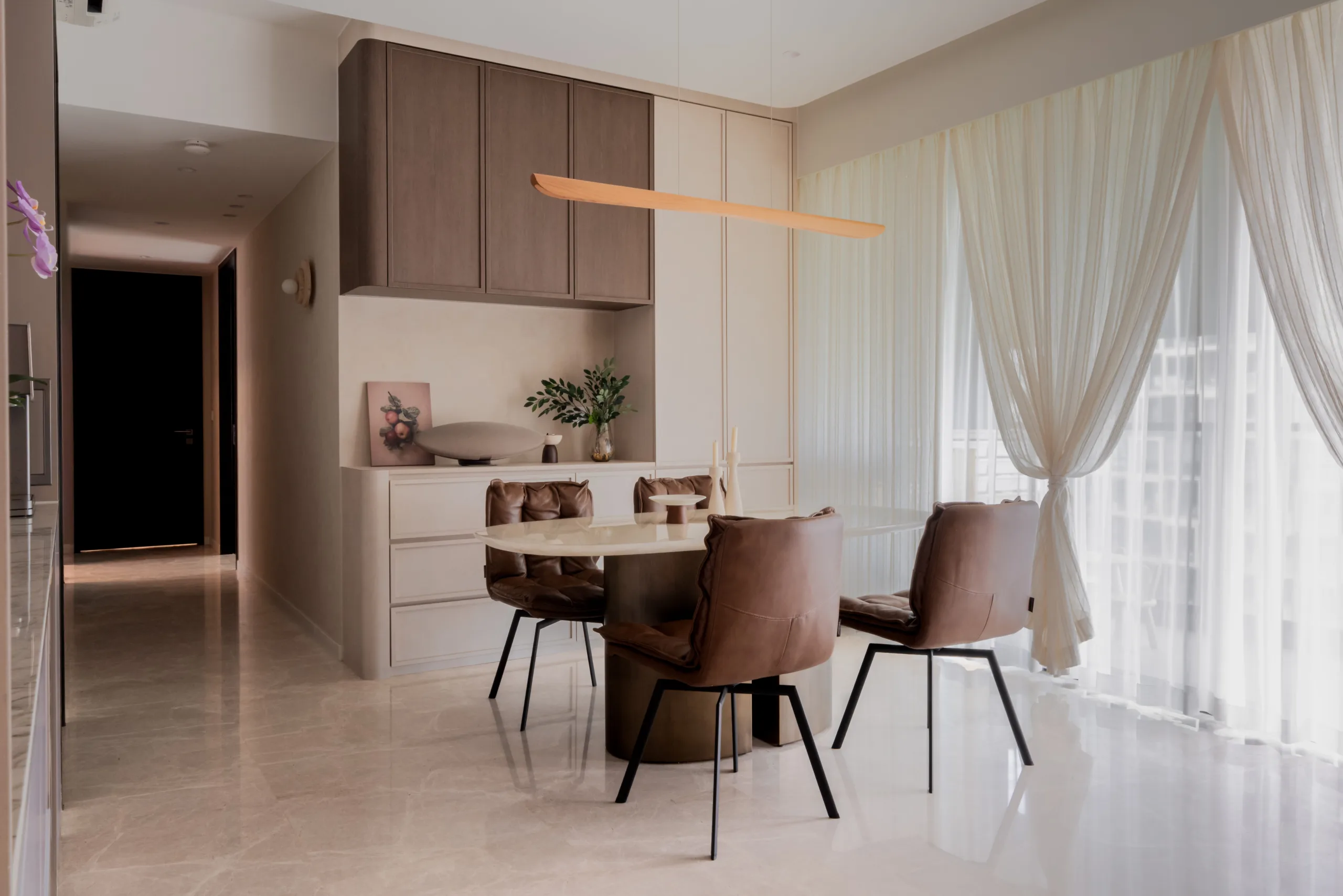 Wabi-sabi dining and living area with an oval stone table, brown leather chairs and a sweeping linear timber pendant light