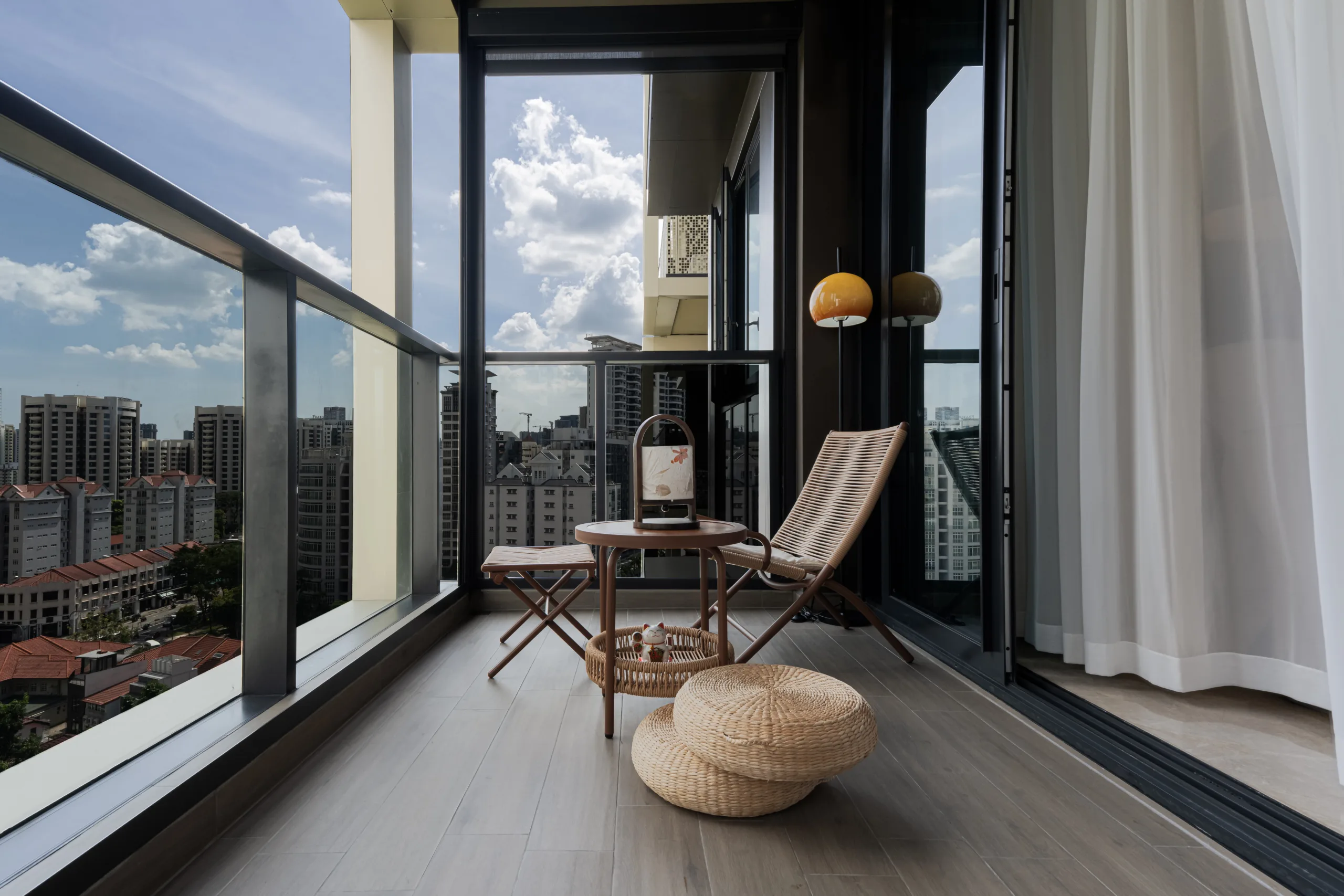 High-floor balcony of a wabi-sabi condo at Irwell Hill Residences with a rattan lounge chair and a Singapore city skyline view