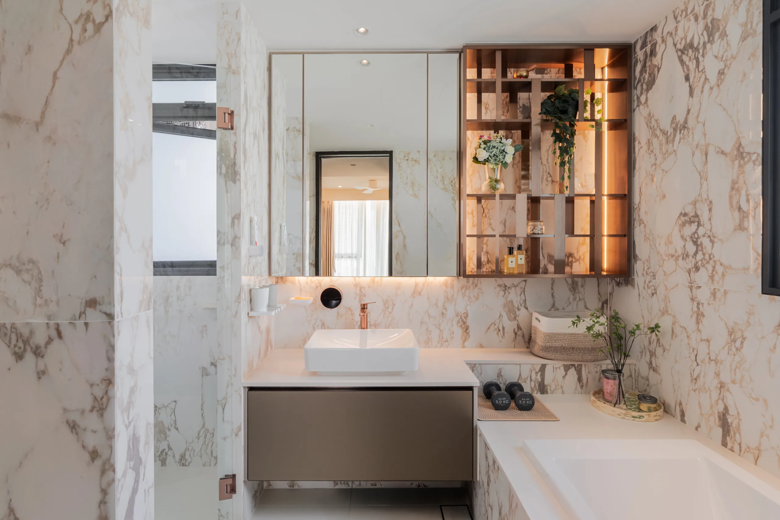 Wabi-sabi master bathroom in gold-veined marble with a vessel basin, rose-gold tap and a back-lit bronze display niche