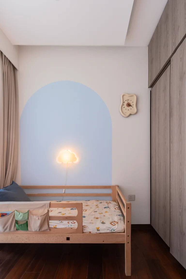 Children's bedroom with a soft blue painted arch, cloud-shaped wall lamp and a light oak wardrobe in a wabi-sabi condo