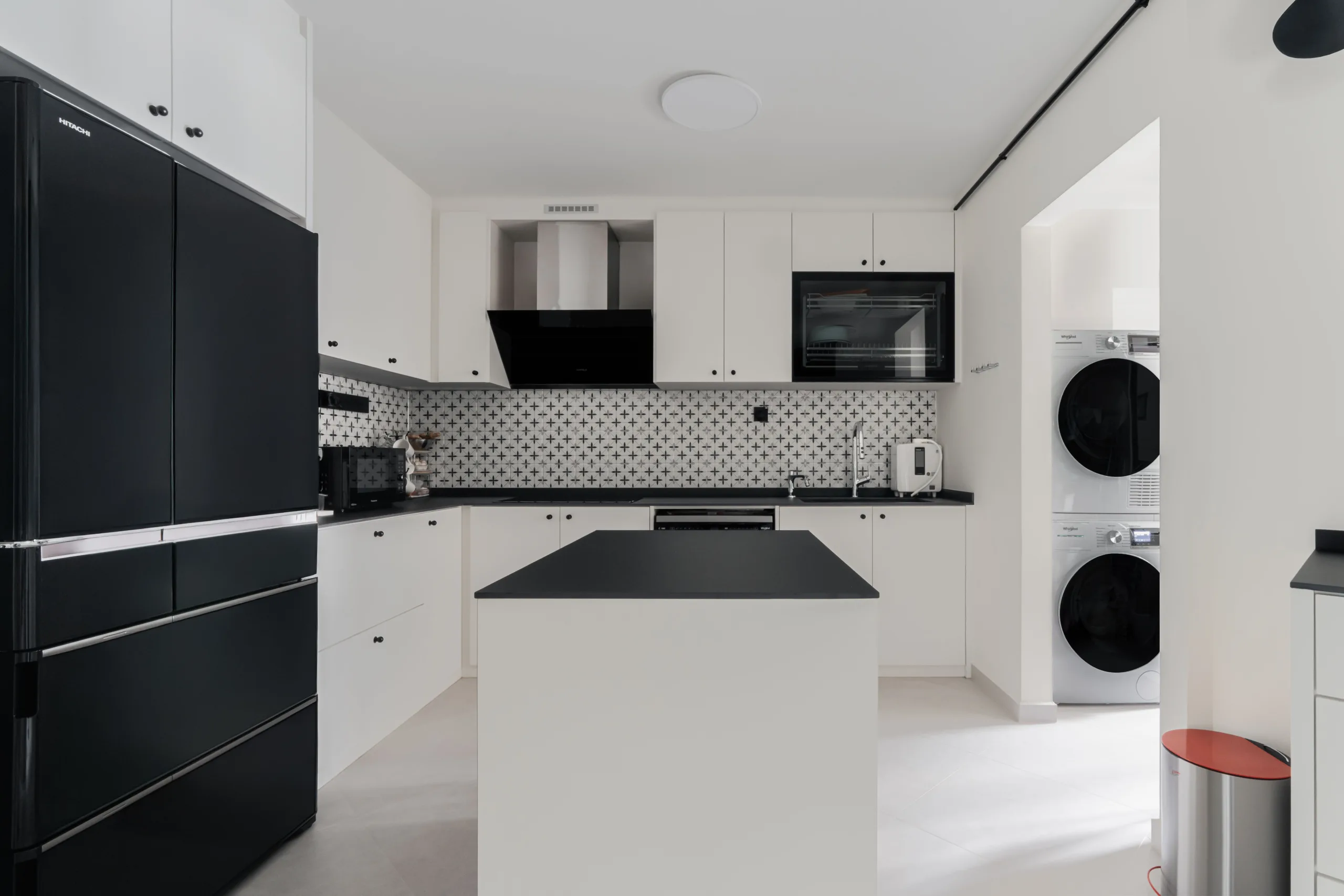 Kitchen appliance wall with black fridge, chimney hood and stacked washer-dryer in the service yard