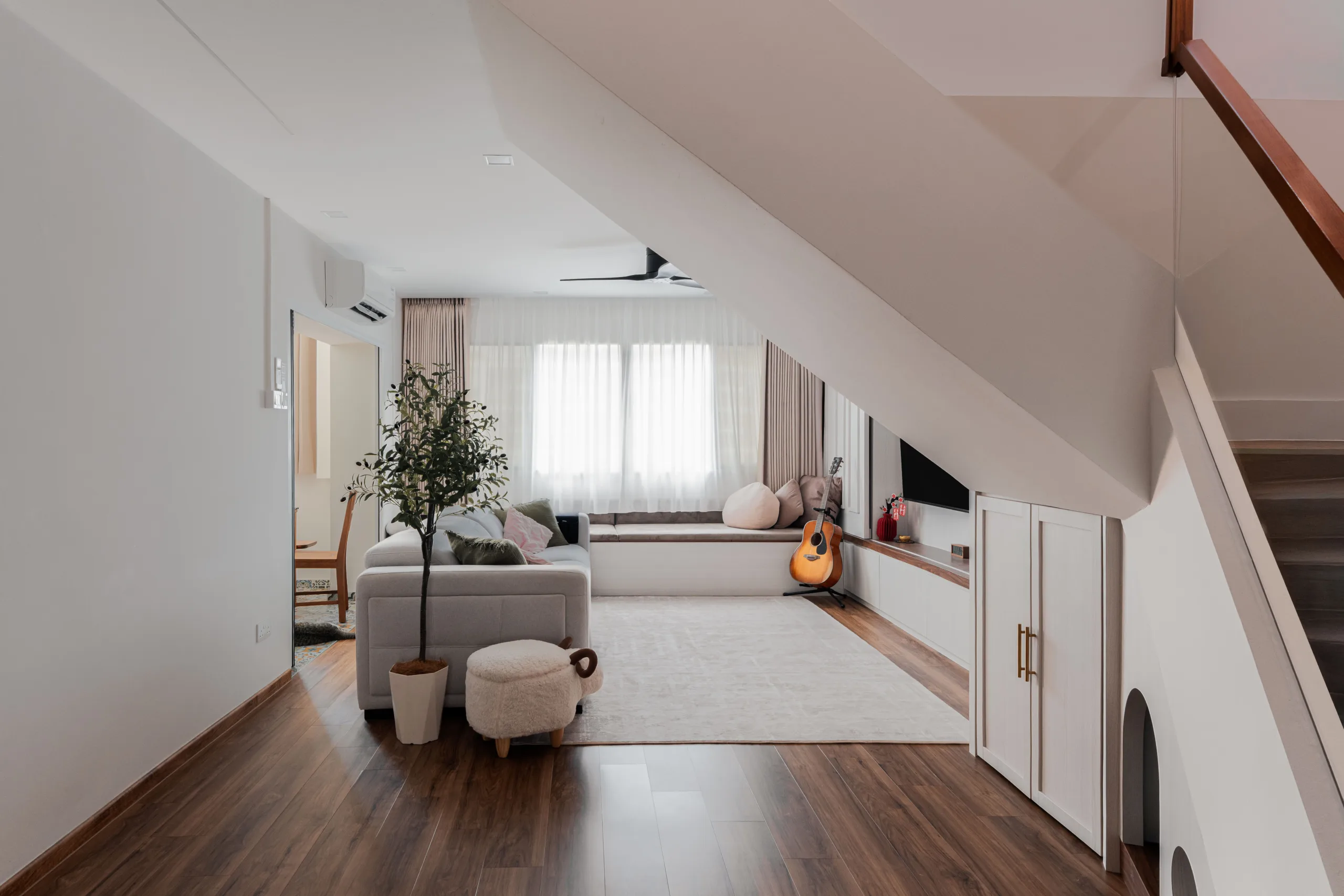 Open upper living room under the sloping stair soffit, looking towards the window seat
