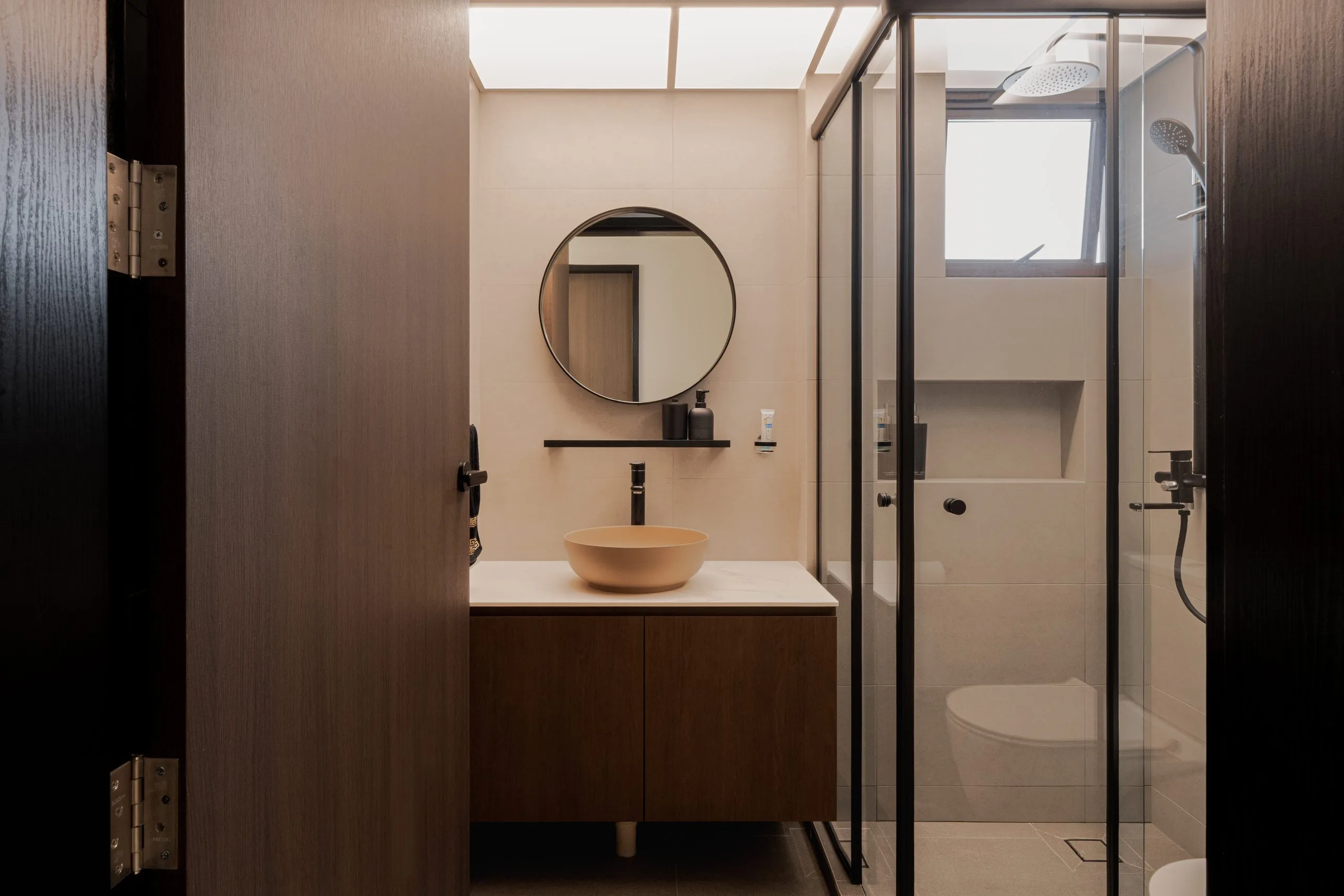 Bathroom with a round mirror, a bowl basin on a timber vanity and a black-framed glass shower screen