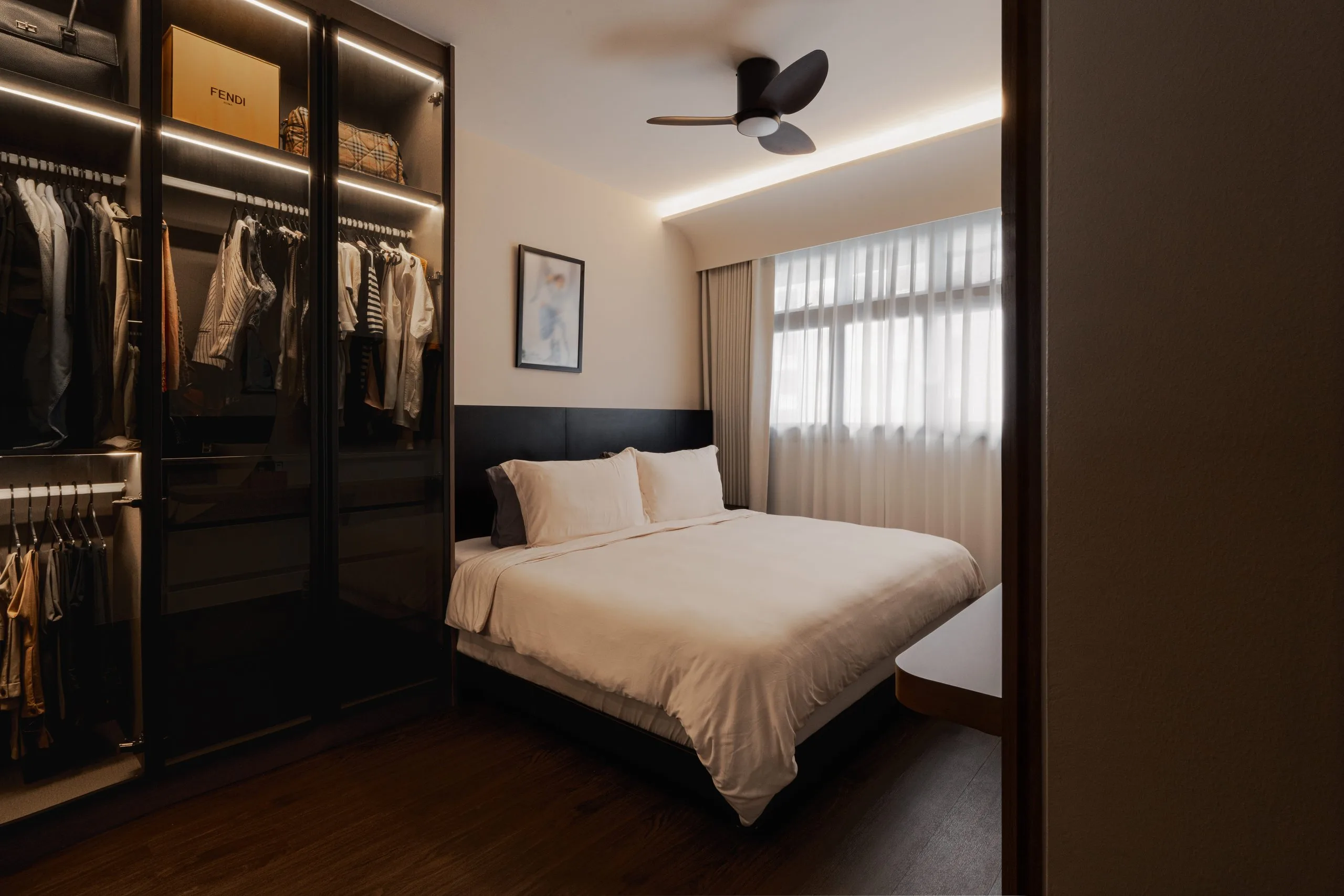 Bedroom with a dark glass-door wardrobe with internal lighting, a dark headboard and cove lighting
