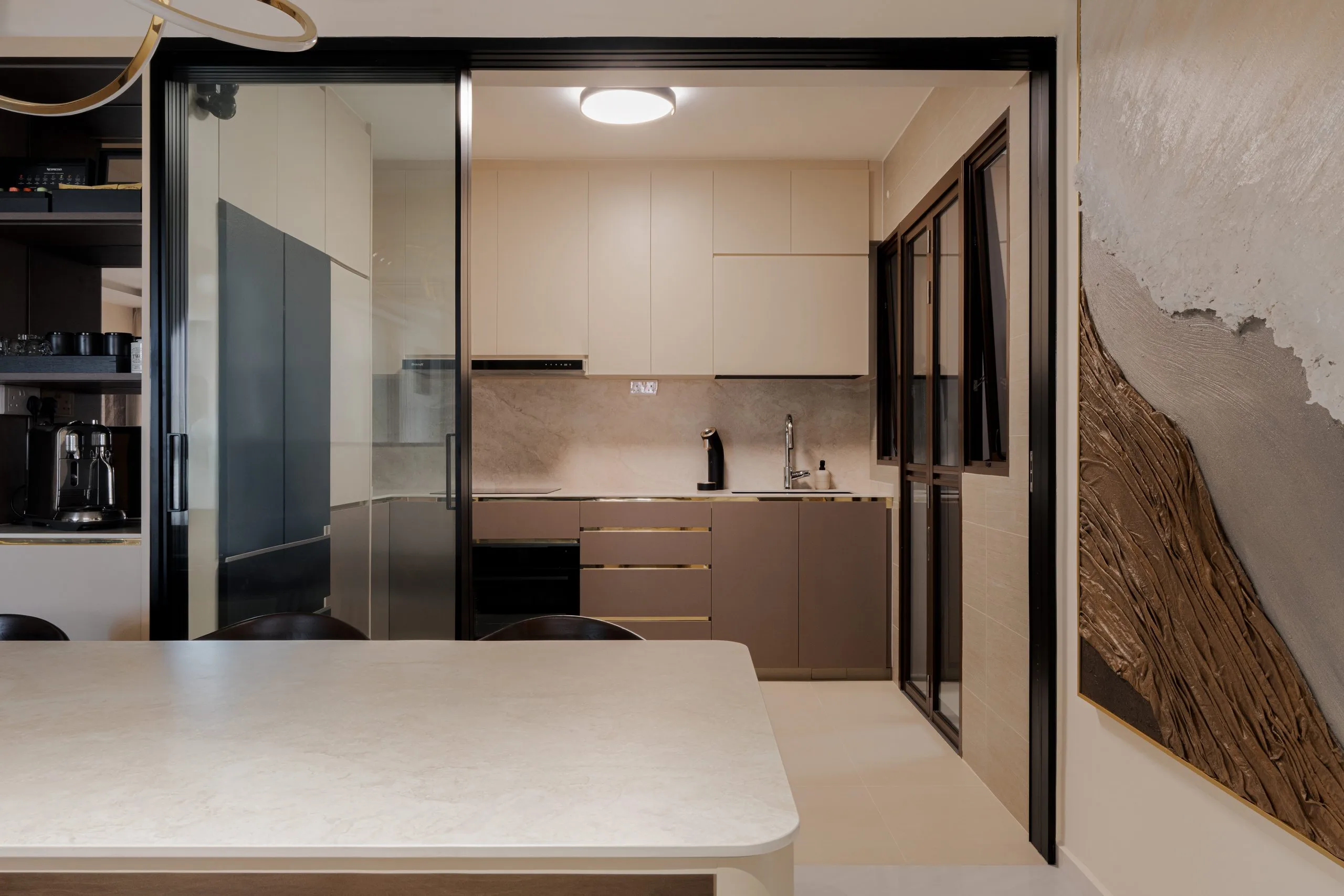 Kitchen with cream upper cabinets, taupe base cabinets and a stone-look backsplash behind black-framed glass sliding doors