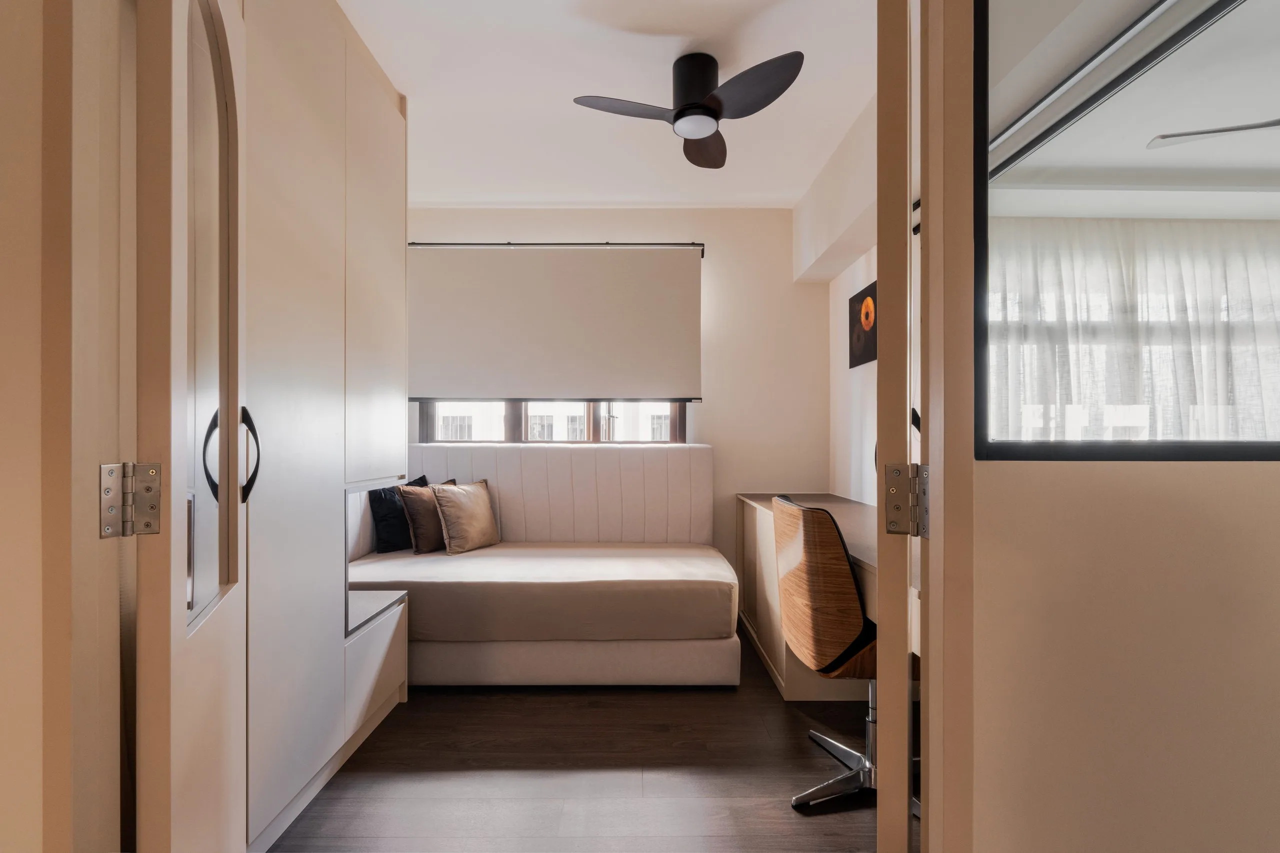 Room with an upholstered daybed under the window, a built-in desk and a wardrobe with an arched glass door panel
