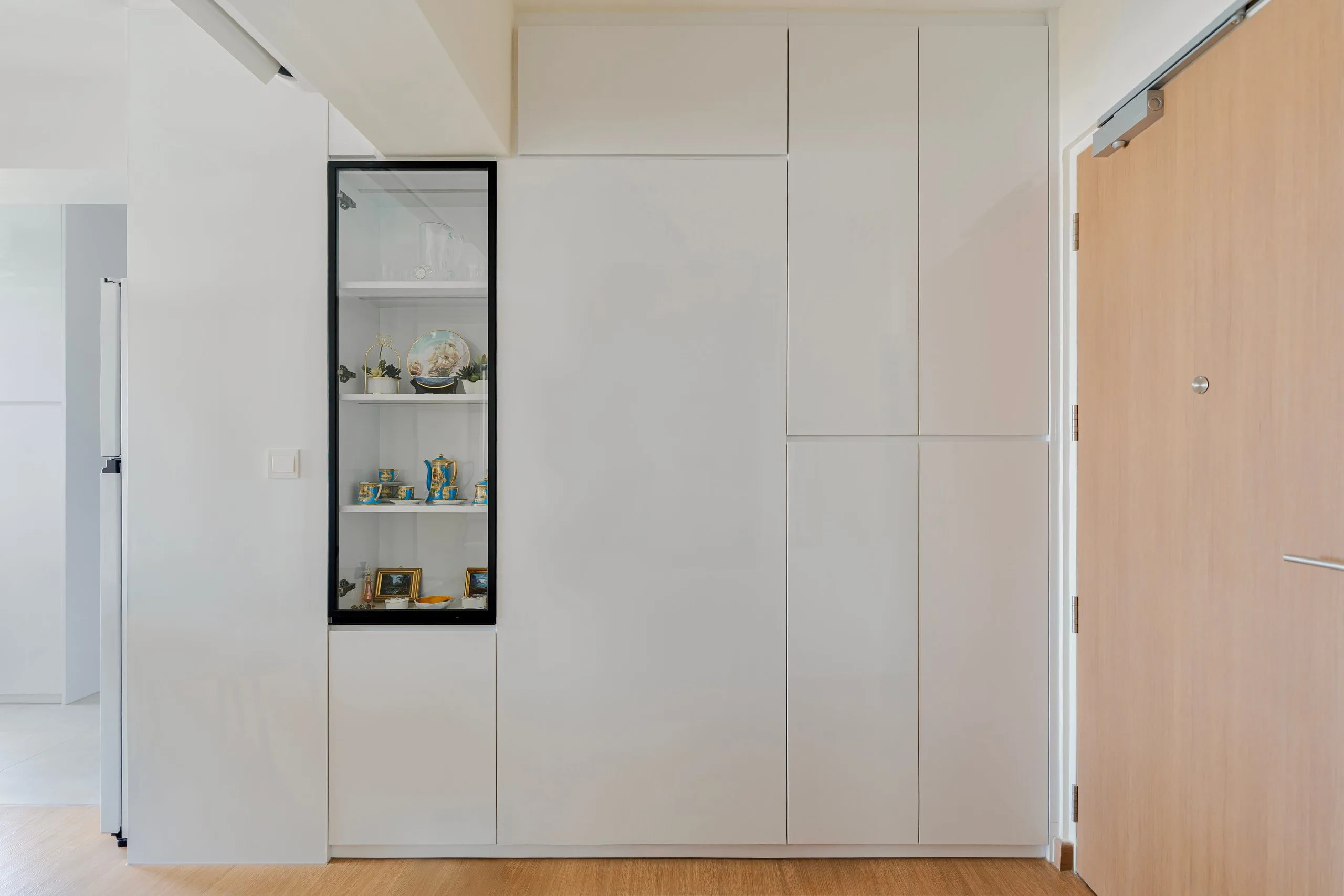 Wall of white full-height cabinets with a black-framed glass display section, beside a timber-look sliding door
