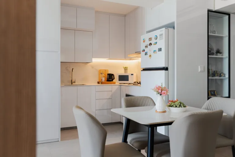 White kitchen cabinets with a lit worktop behind a four-seat dining table, beside a glass-door display cabinet