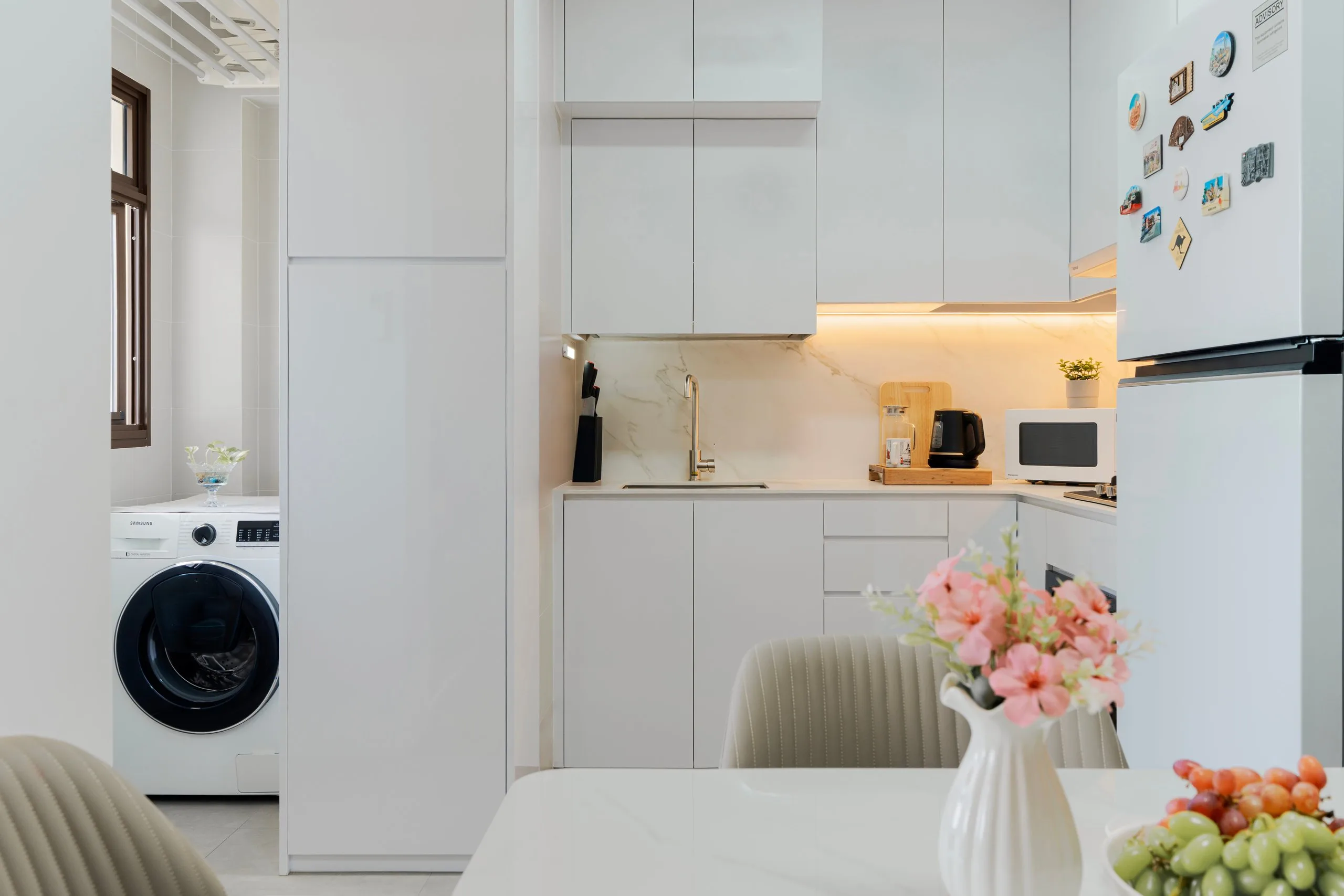 L-shaped kitchen with white handle-free cabinets, a marble-look backsplash and under-cabinet lighting
