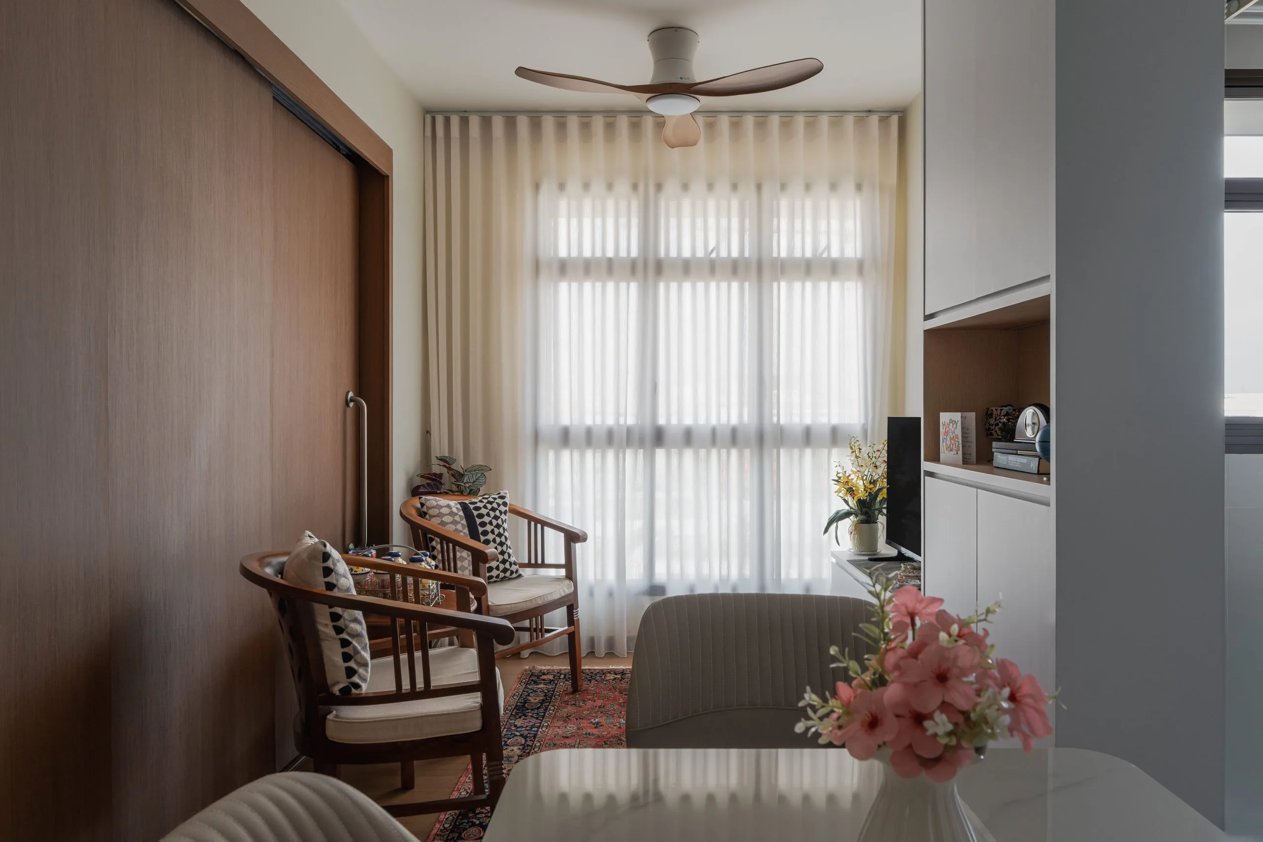 Living area with two timber armchairs, sheer curtains and a full-height timber-look sliding partition
