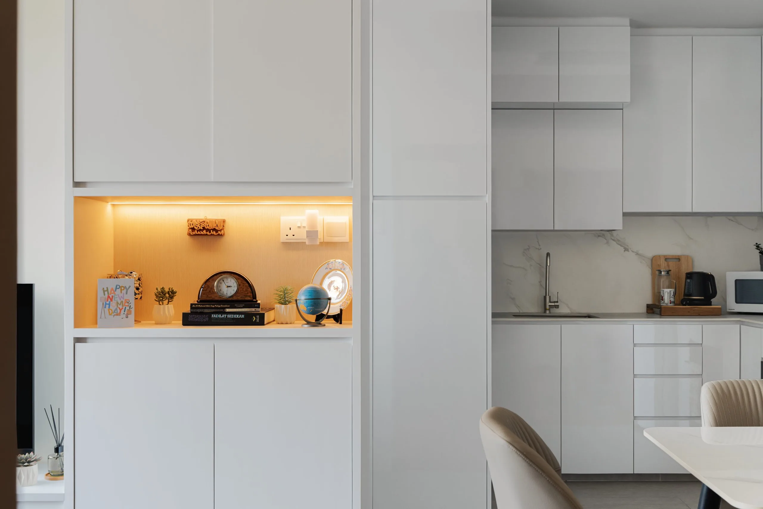 White full-height cabinets with a timber-lined open niche lit from above, next to the kitchen