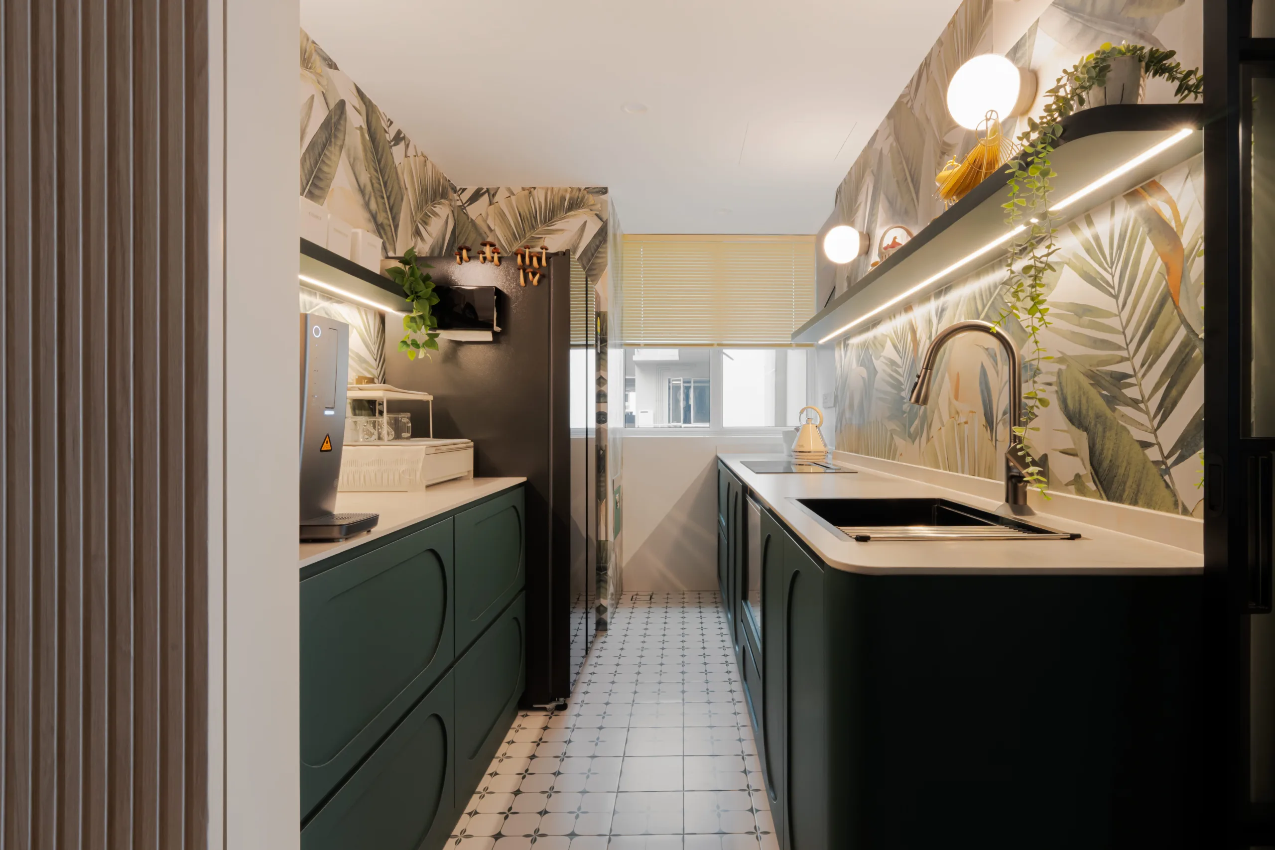 Galley kitchen at Watercolours EC with forest green arch-front cabinetry, patterned encaustic floor tiles and a tropical botanical feature wall