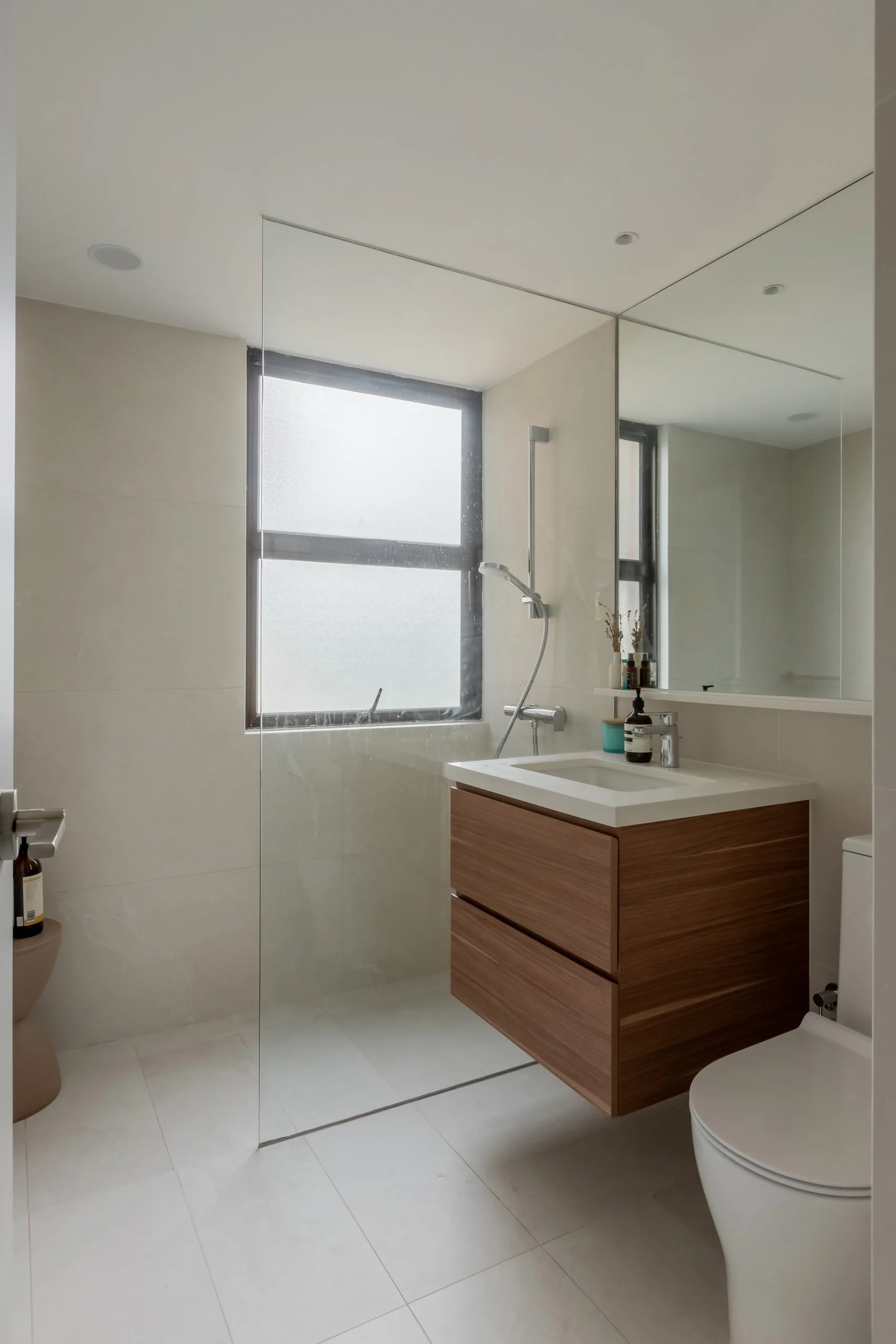 Bathroom with a wood-toned floating vanity, a frameless glass shower screen and pale stone-look wall tiles