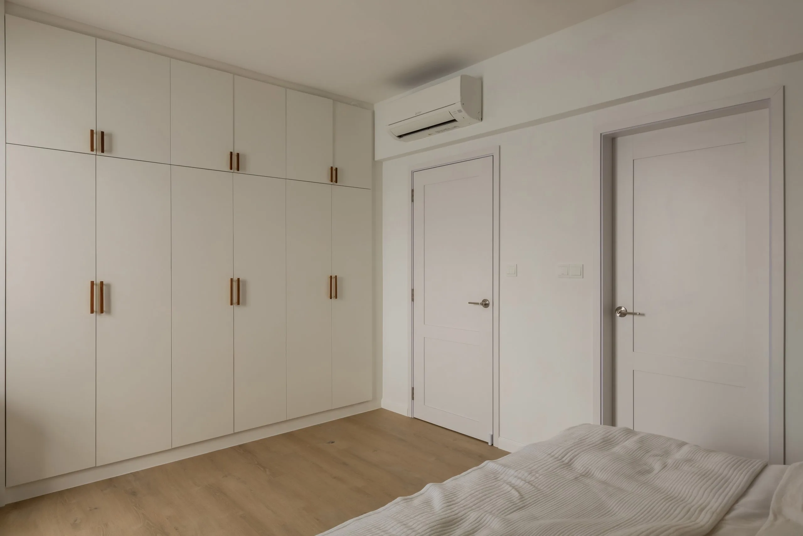 Bedroom with a wall of full-height white wardrobes with wood-toned pull handles and timber-look flooring