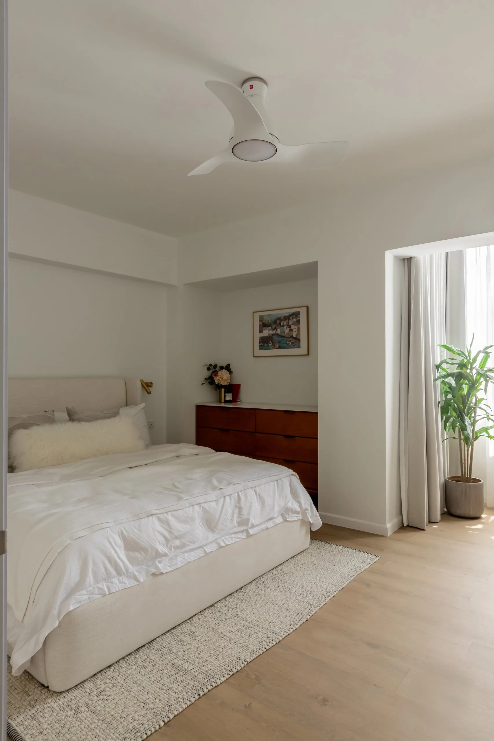 Bedroom with an upholstered bed, a wood-toned chest of drawers in a wall recess and a curtained window bay