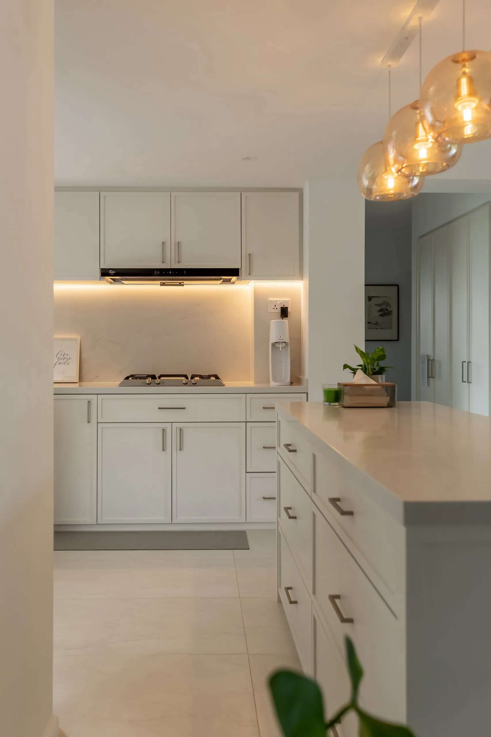 Side view of the kitchen with white framed cabinet doors, warm under-cabinet lights over the hob and the peninsula in the foreground