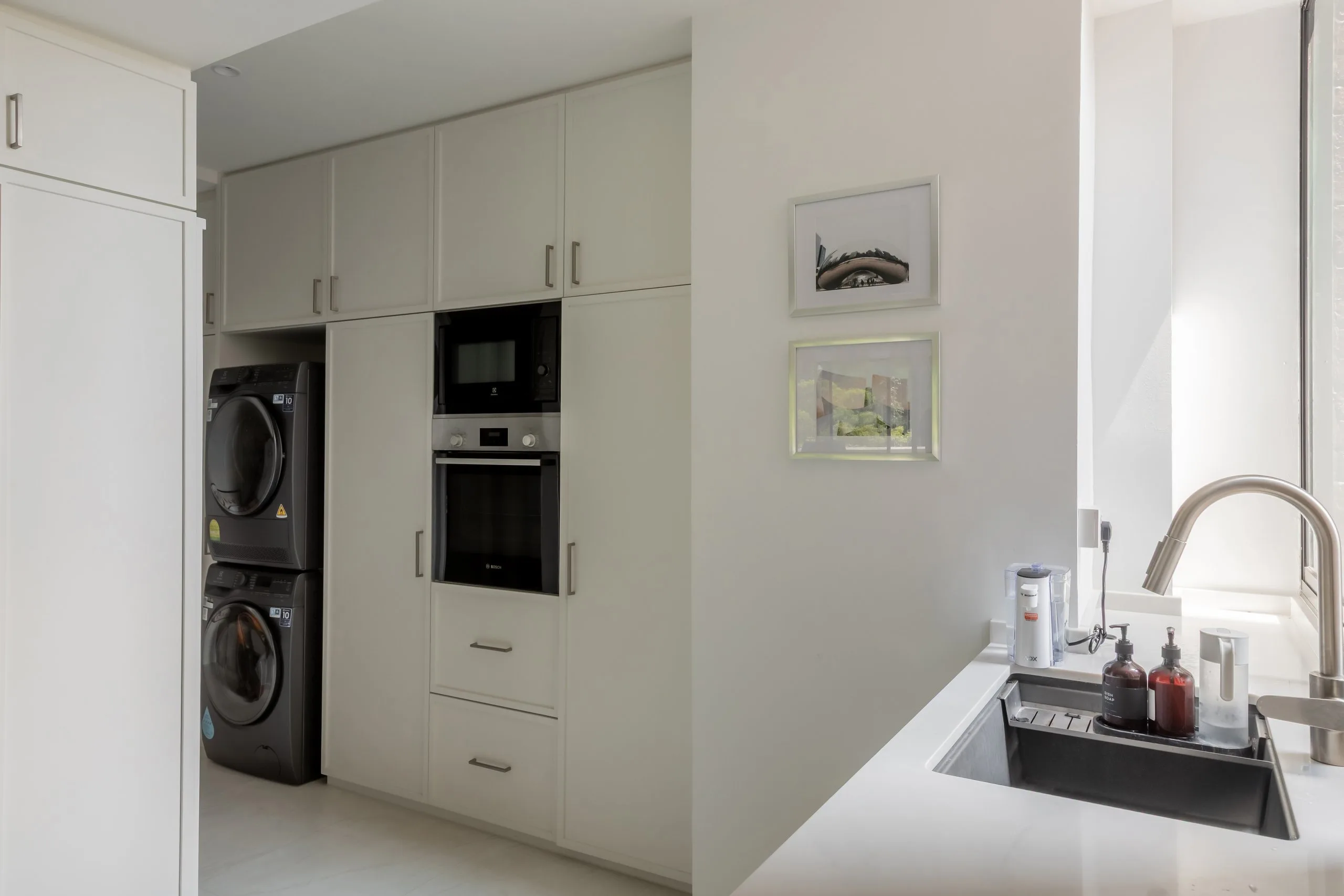 Full-height white cabinets around a stacked washer and dryer and a built-in oven and microwave, beside the kitchen sink