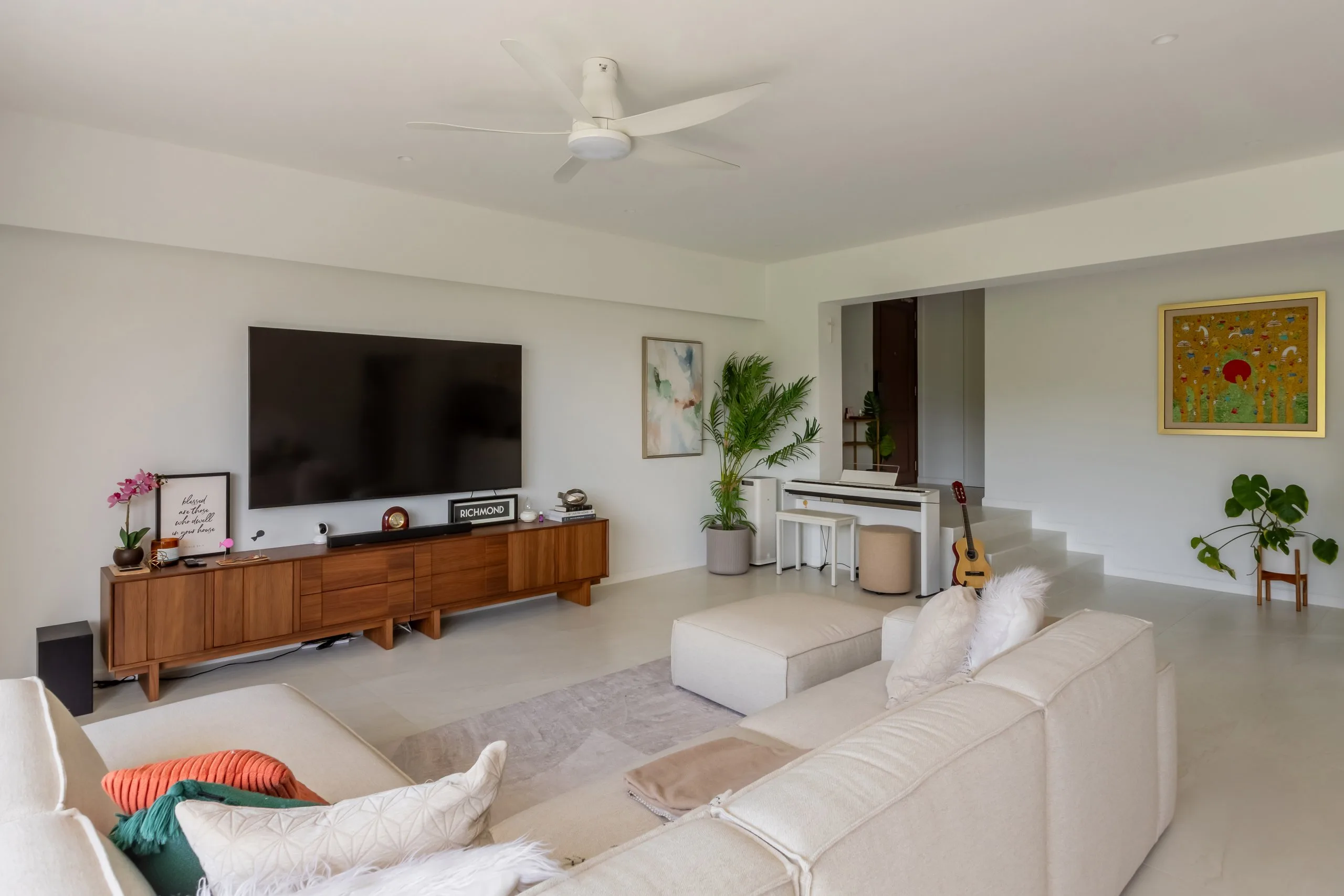 Wide view of the living room with a wood-toned TV console, a white digital piano and tiled steps up to a raised corridor